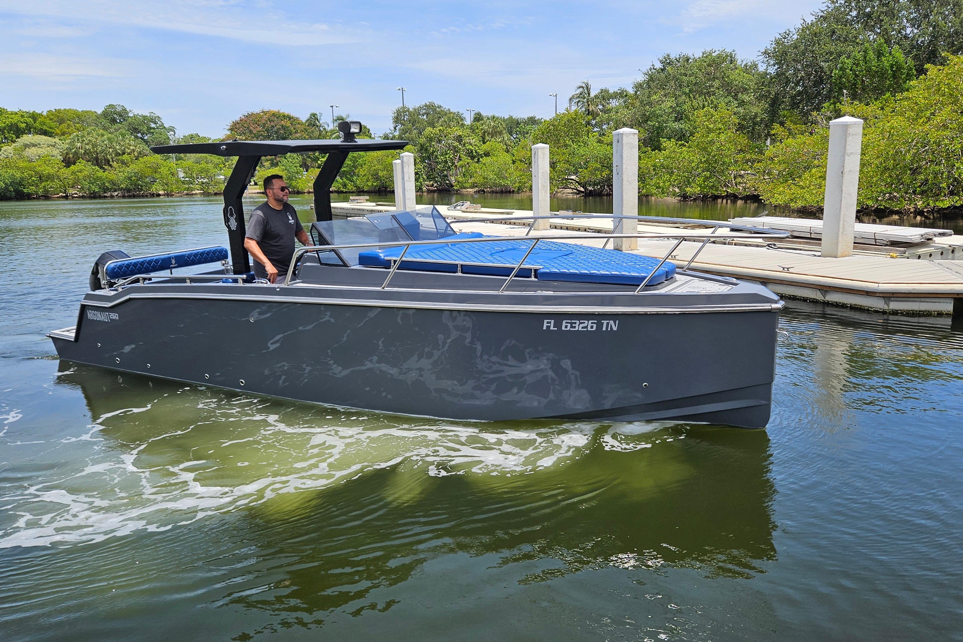 2023 Argonaut 260 boat cruising near a dock, surrounded by lush greenery.