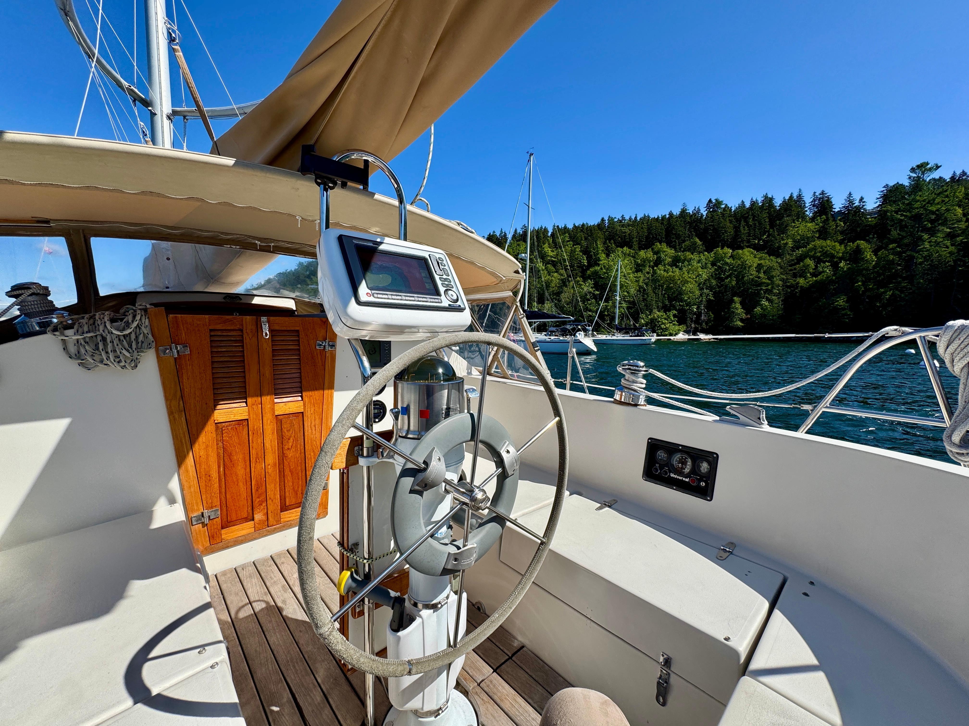 1989 Nonsuch 30 Ultra sailboat cockpit with steering wheel, navigation equipment, and scenic water view.