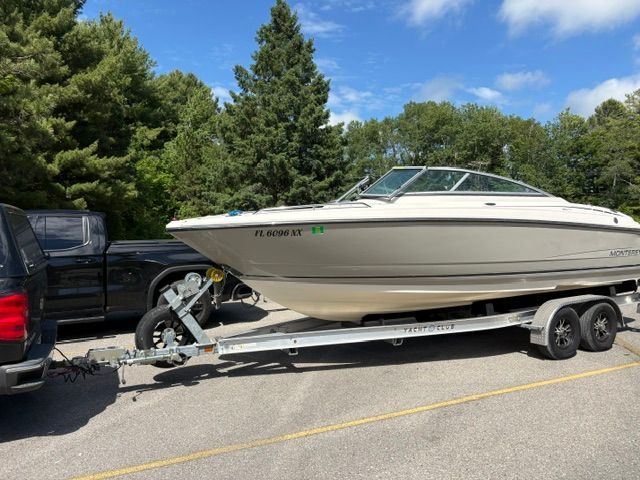 A 2009 Monterey 234FS boat on a trailer, parked next to a black vehicle.