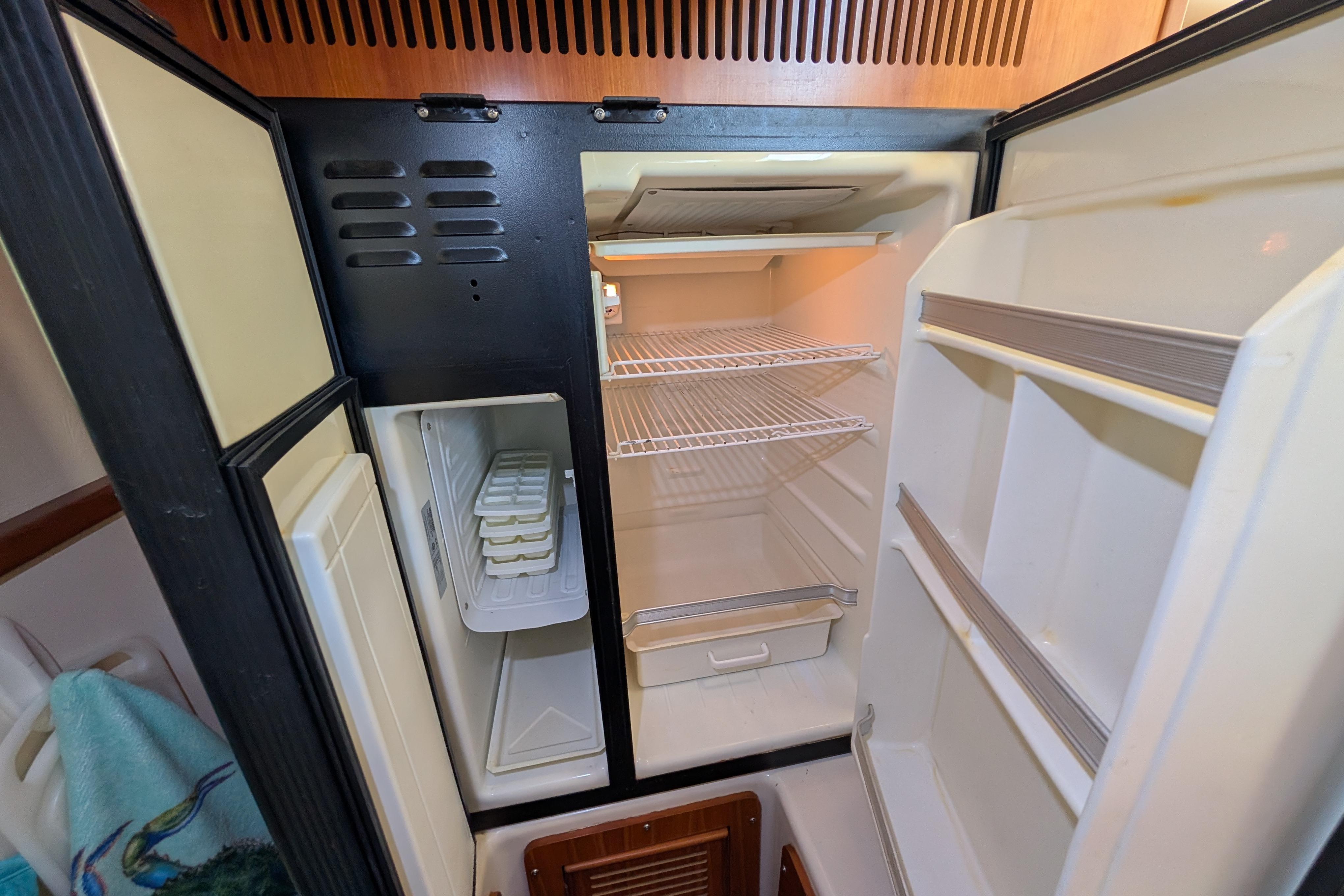 Open refrigerator inside 2004 PDQ 34 Powercat, featuring empty shelves and ice trays.