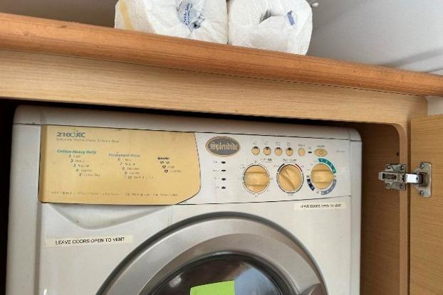 Washing machine in wooden cabinet on Lagoon 421, 2010 model, with paper towels above.