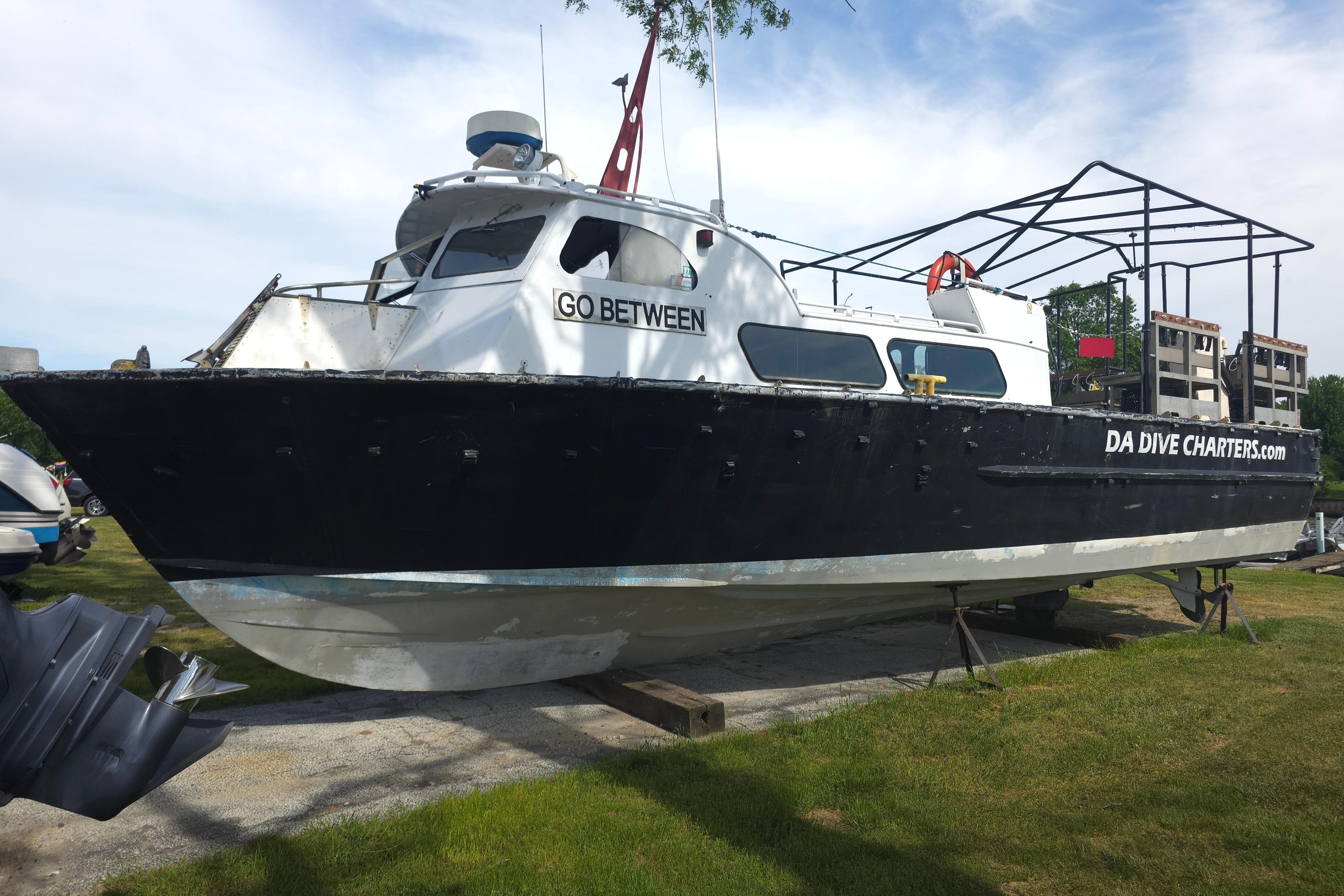 1974 Breaux's Bay Craft passenger boat on land, labeled "GO BETWEEN" and "DA DIVE CHARTERS.com".