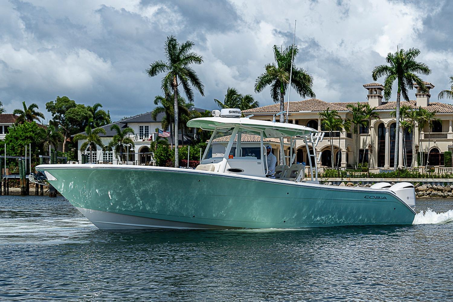2019 Cobia 320 Center Console boat cruising near luxury waterfront homes.