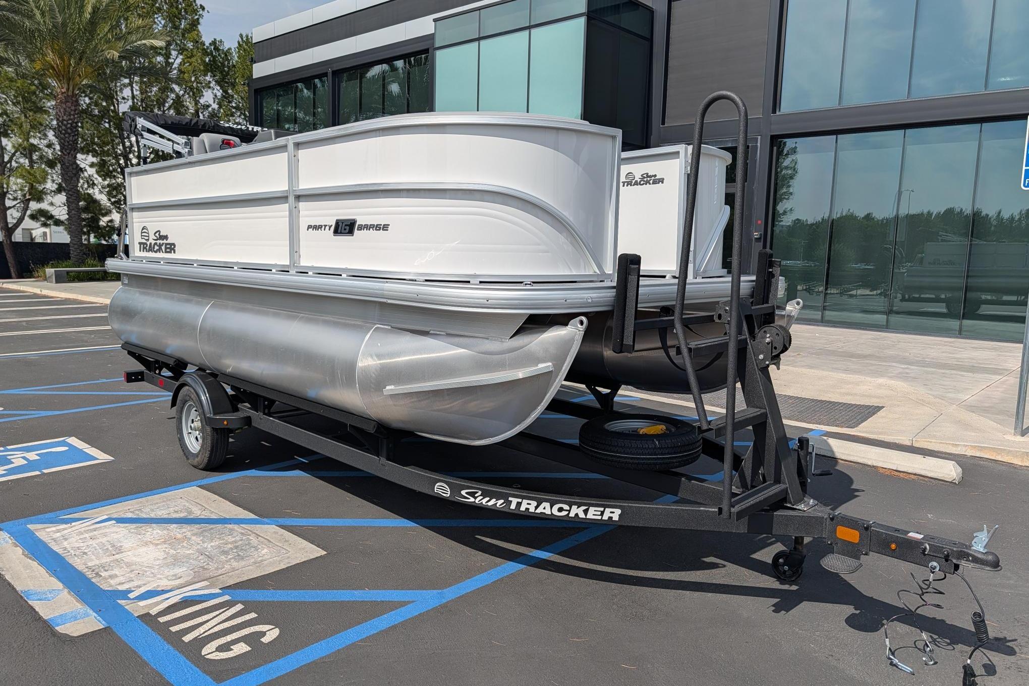 2026 Sun Tracker Party Barge 16 DLX pontoon boat on trailer in parking lot.