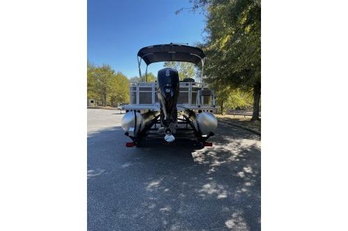 2026 Sun Tracker Fishin' Barge 22 DLX pontoon boat parked under trees.