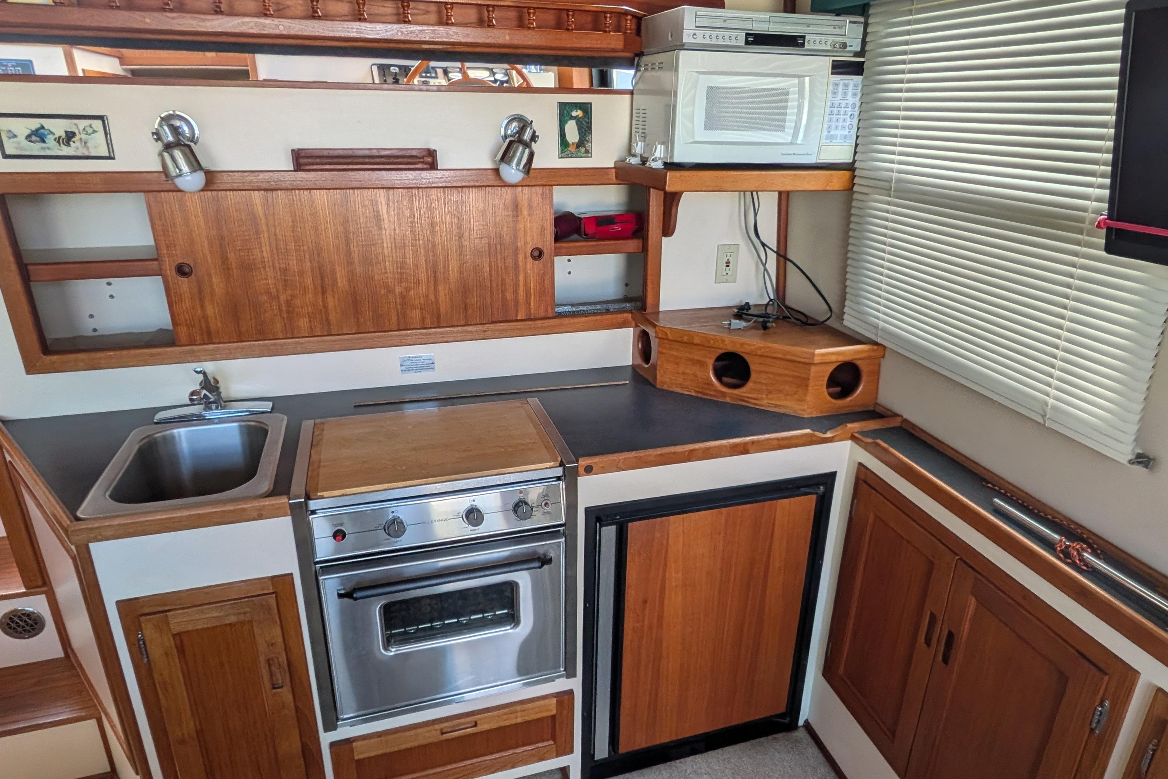 Compact kitchen in a 1998 Nordic Tug 32, featuring wood cabinetry, sink, stove, and microwave.