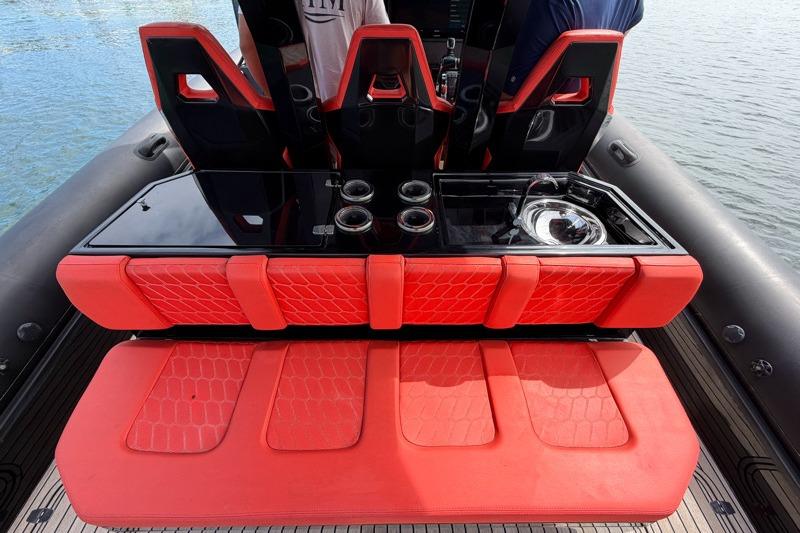 Red seating and console on 2023 Skipper-BSK 42NC boat, featuring sleek design and water backdrop.