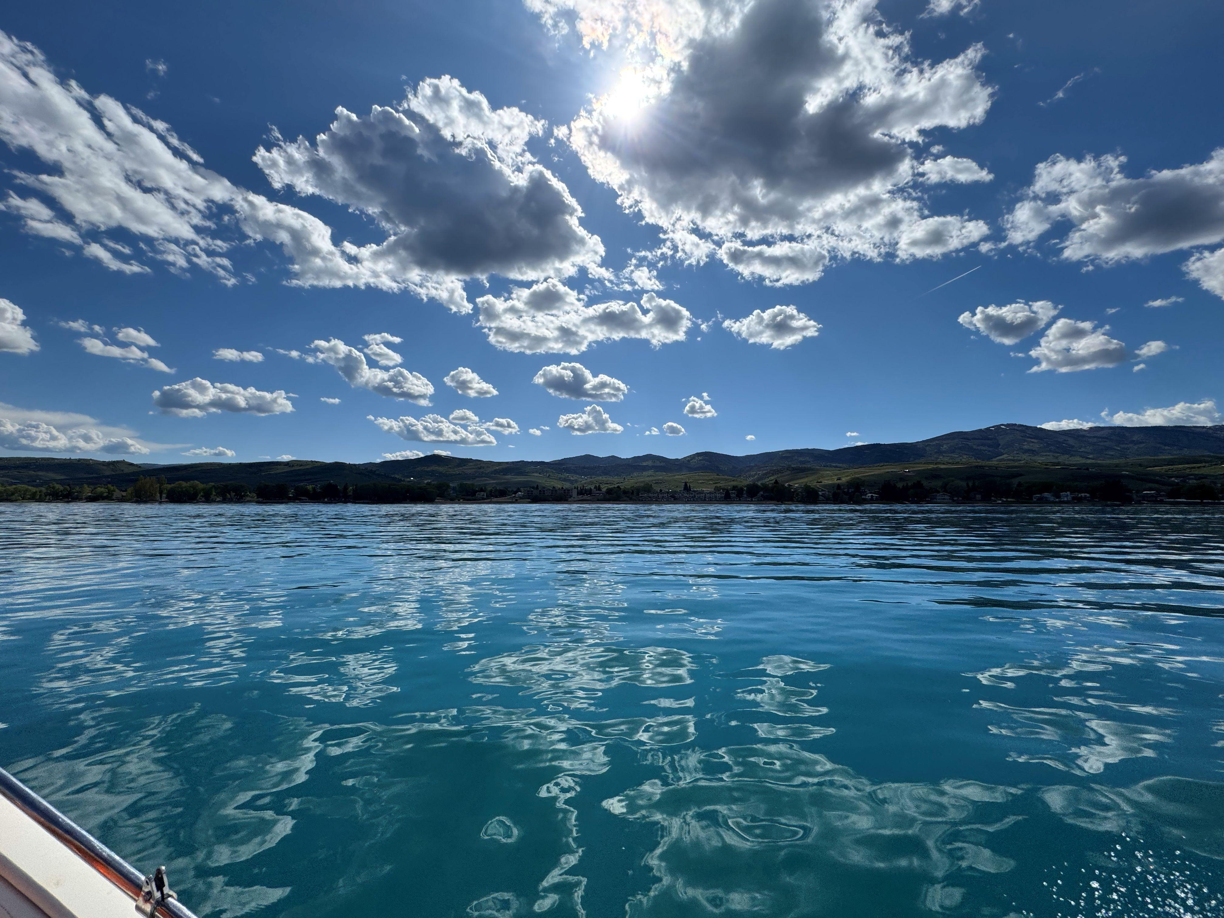 Calm lake under a bright sky with clouds, viewed from a boat.