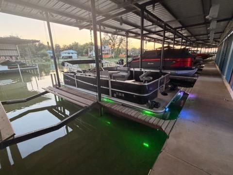 A 2013 Cypress Cay Seabreeze 212 pontoon boat docked under a covered area with colorful lights.