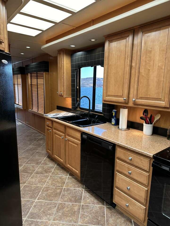 Modern kitchen interior in a 2005 Sumerset Top Hat houseboat, featuring wood cabinets and lake view.