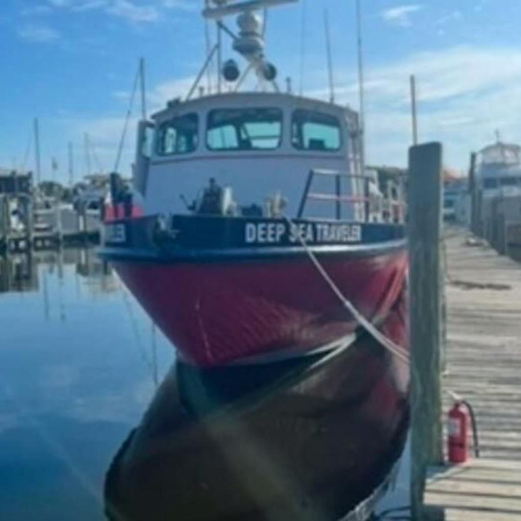 Red and black commercial boat docked at a marina, labeled "Deep Sea Traveler," under clear blue sky.
