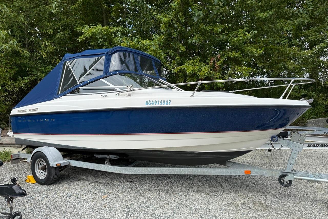 2005 Bayliner 210 Discovery boat on trailer, blue and white, parked outdoors.