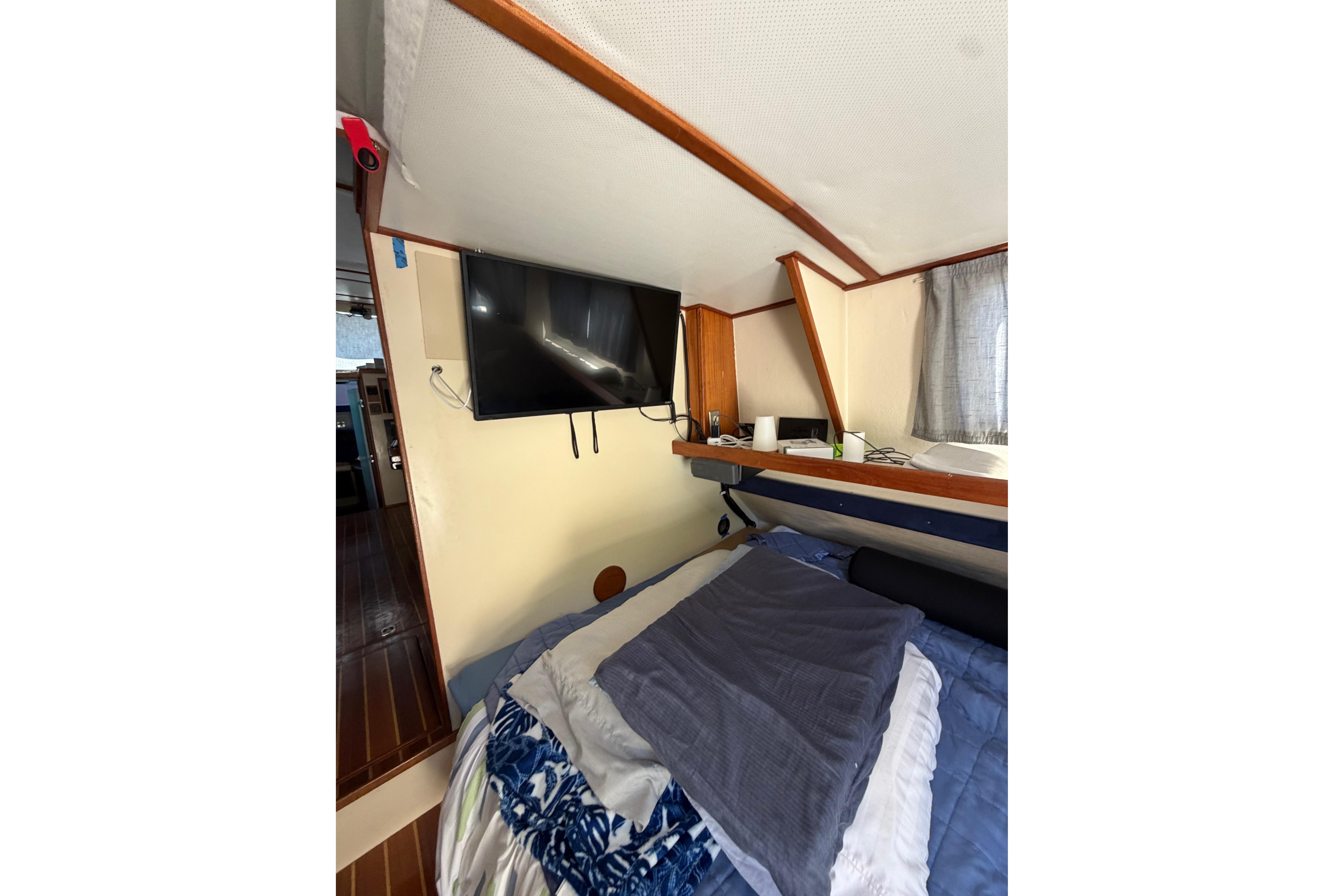 Cozy cabin interior of a 1997 Rosborough Trawler with bed, TV, and wooden accents.