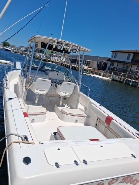 A white boat with two seats and a helm, docked at a pier.