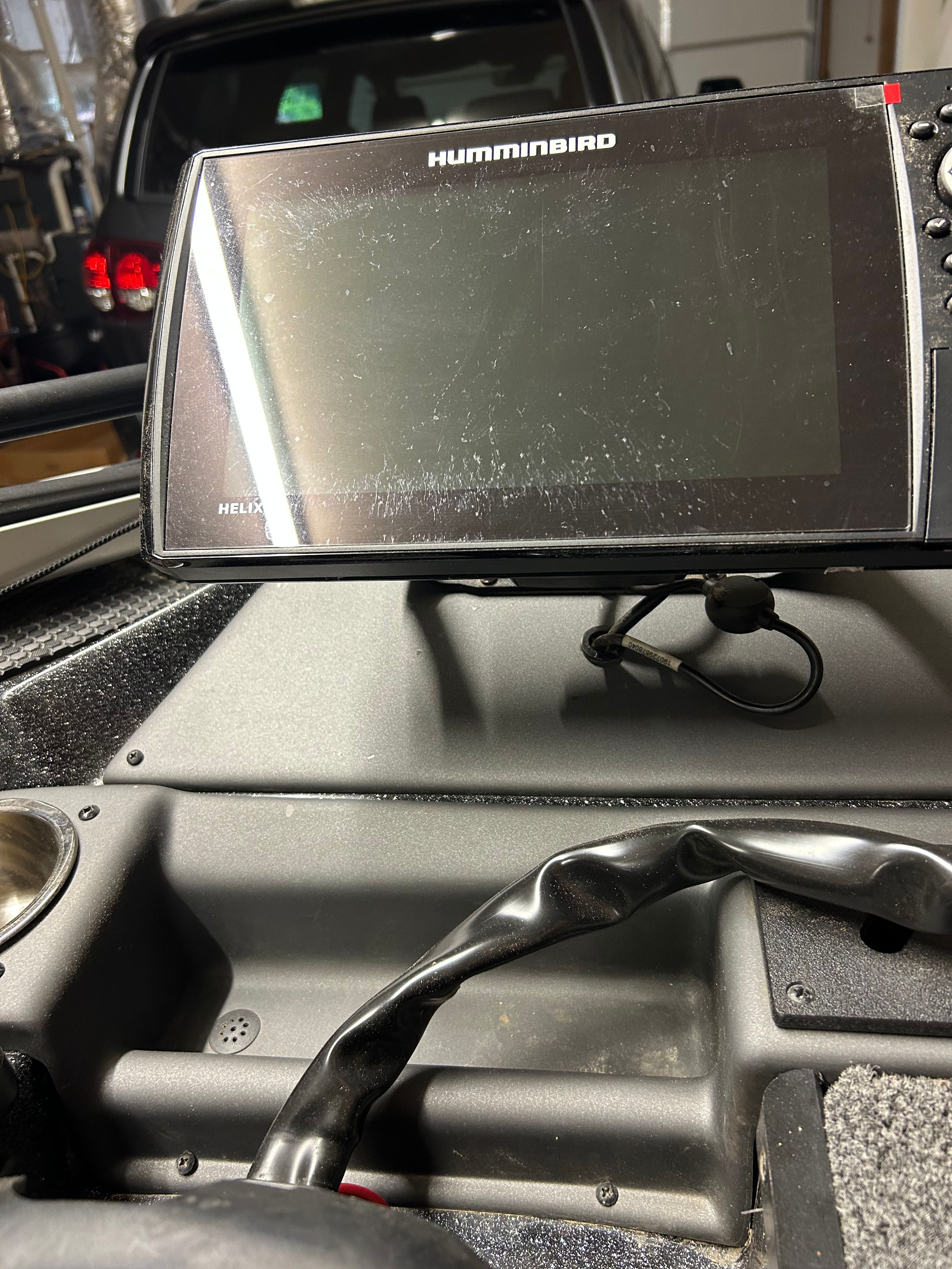 A Humminbird fish finder is mounted on a boat, surrounded by black dashboard and cables.