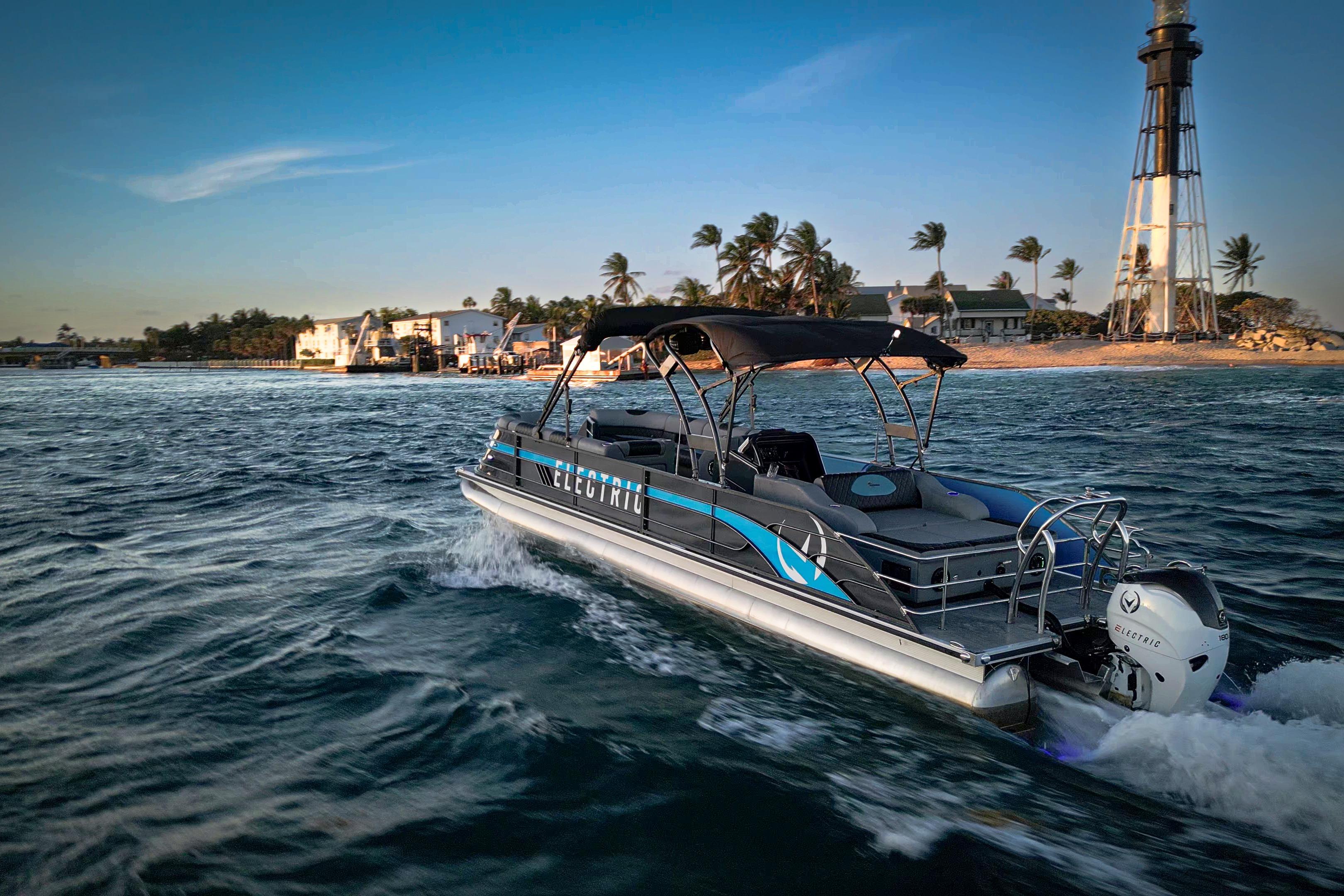 2025 Vision Marine Technologies V30 electric boat cruising near a lighthouse at sunset.