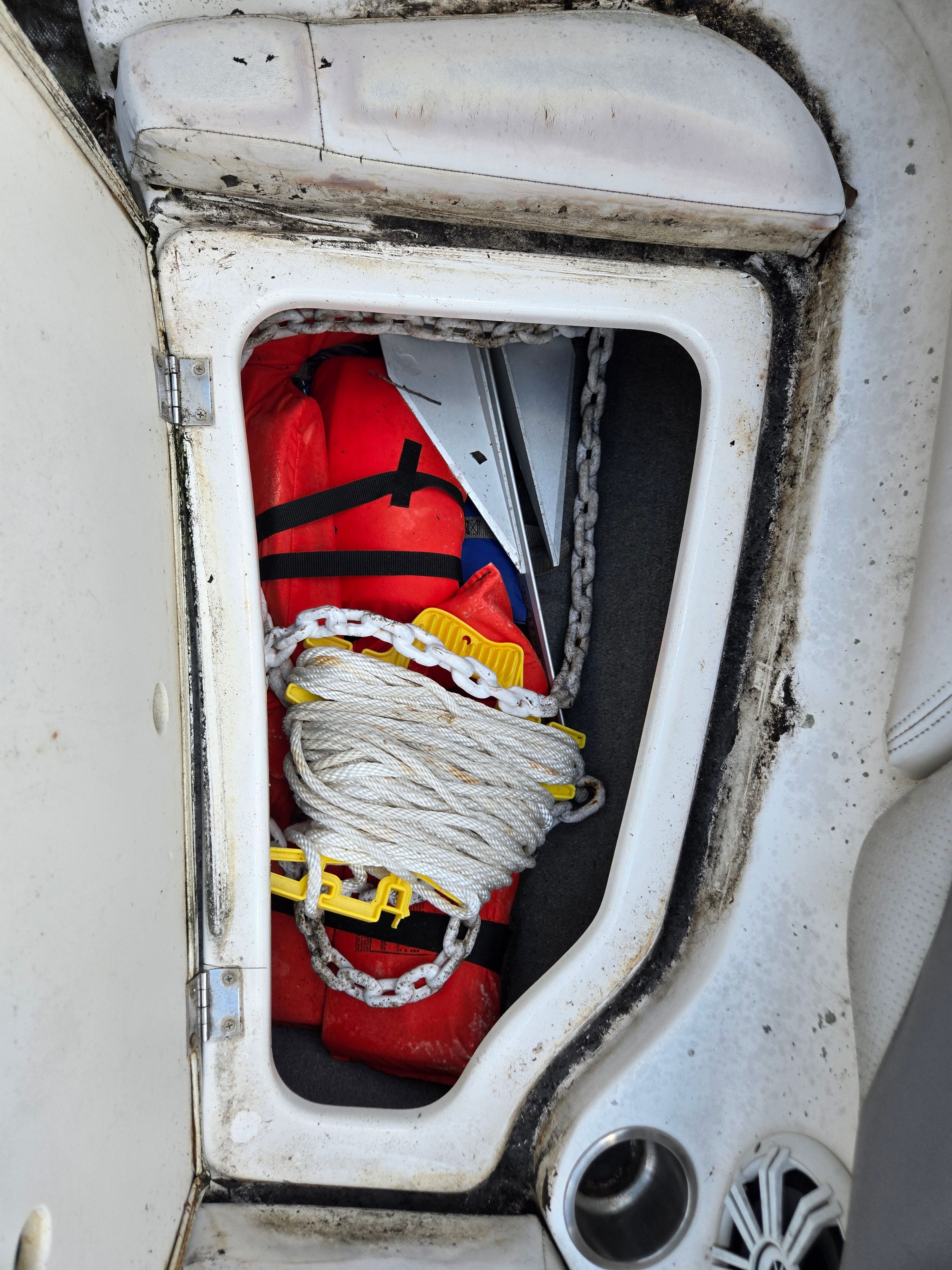 A storage compartment in a boat with life jackets, a rope, and an anchor.