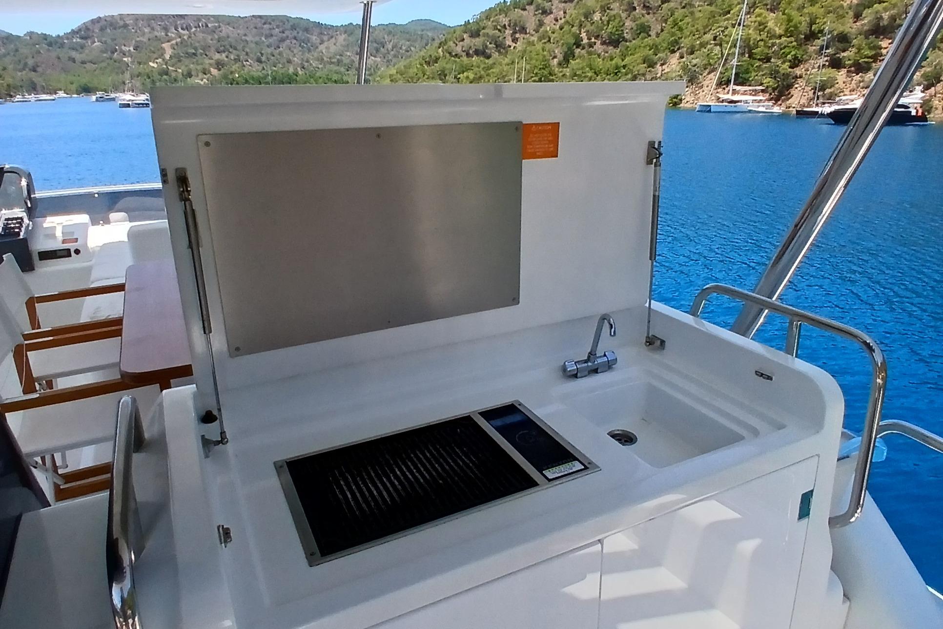Outdoor kitchen on 2022 Sirena 58 yacht with sink and grill, overlooking scenic bay.