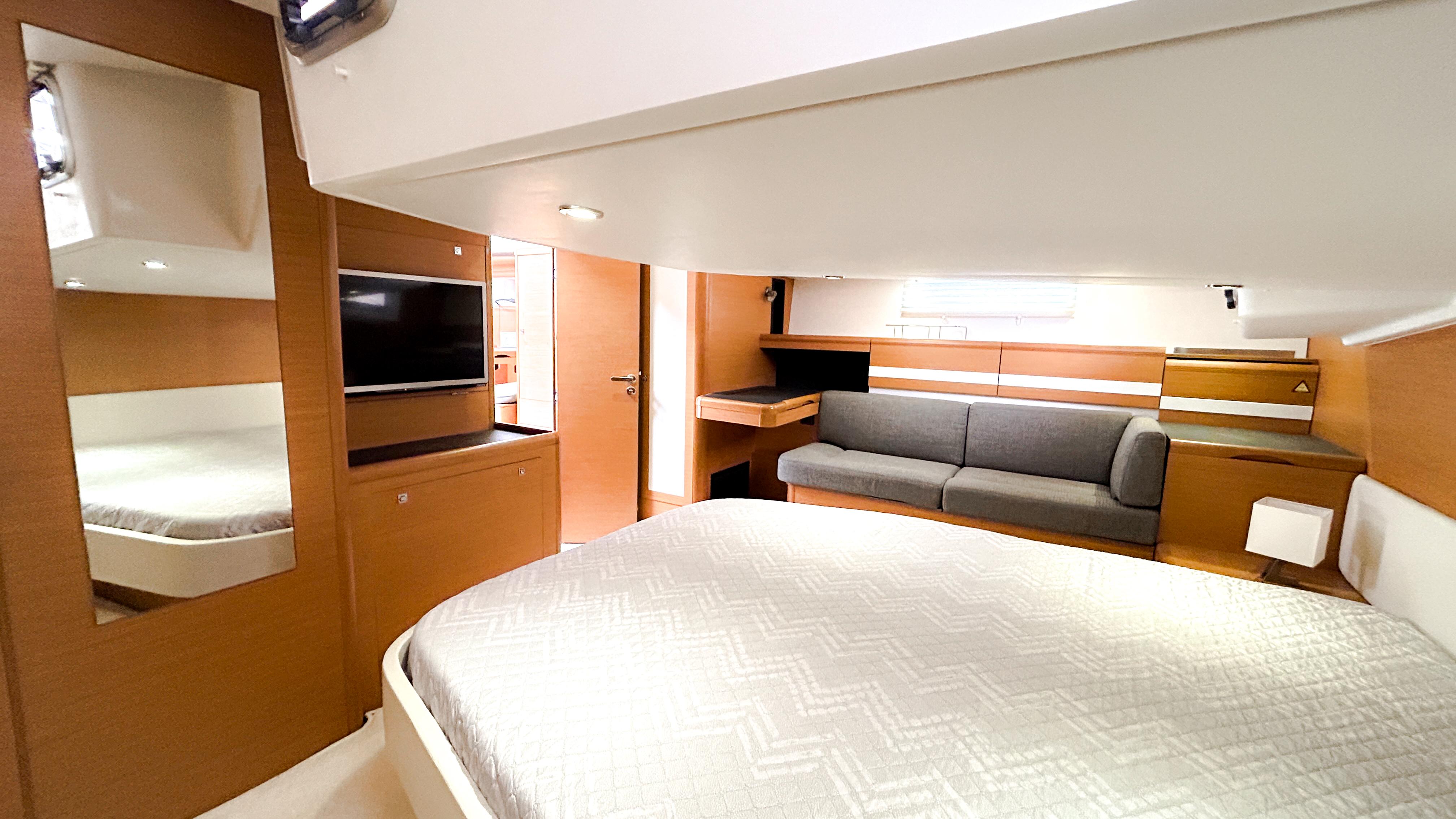 Luxurious interior of 2012 Jeanneau 57 yacht with bed, sofa, and TV.