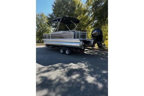 2026 Sun Tracker Fishin' Barge 22 DLX pontoon boat on trailer, parked outdoors.