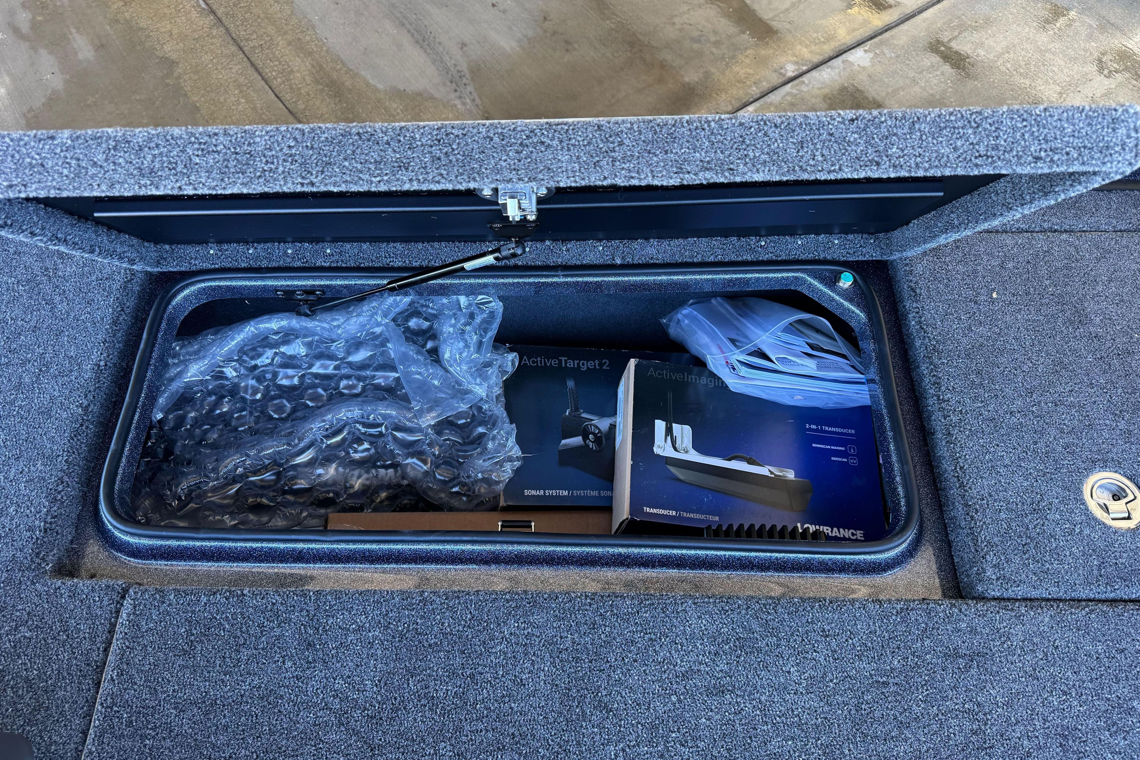 Storage compartment in 2026 Triton 21XP Patriot boat with sonar equipment and packaging.