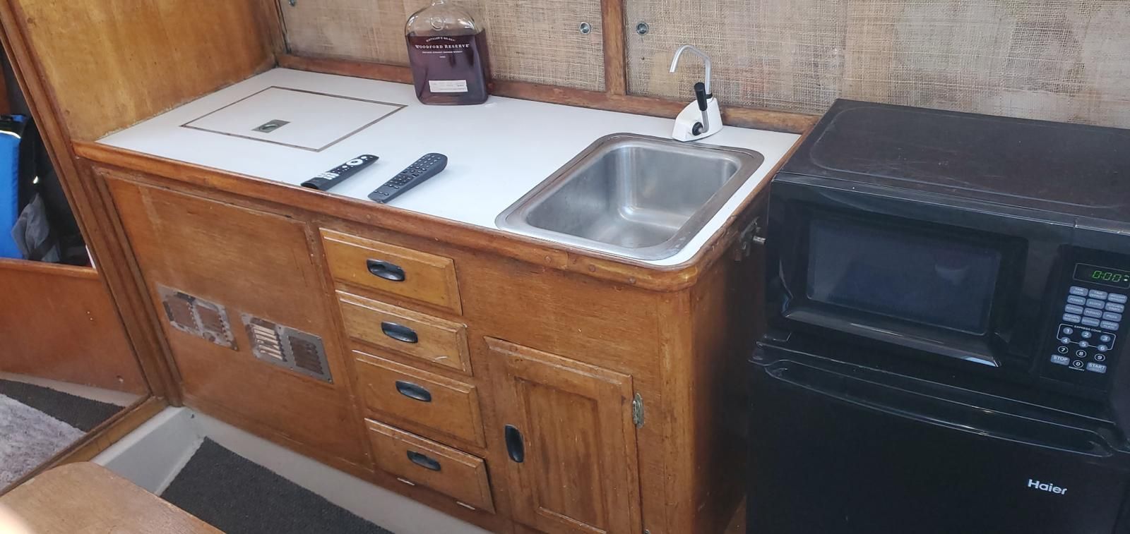 Interior of a boat kitchen with sink, microwave, and wooden cabinets.