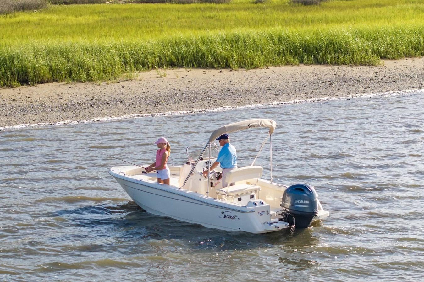 2026 Scout 188 Sportfish boat on water near grassy shoreline, featuring two people fishing.