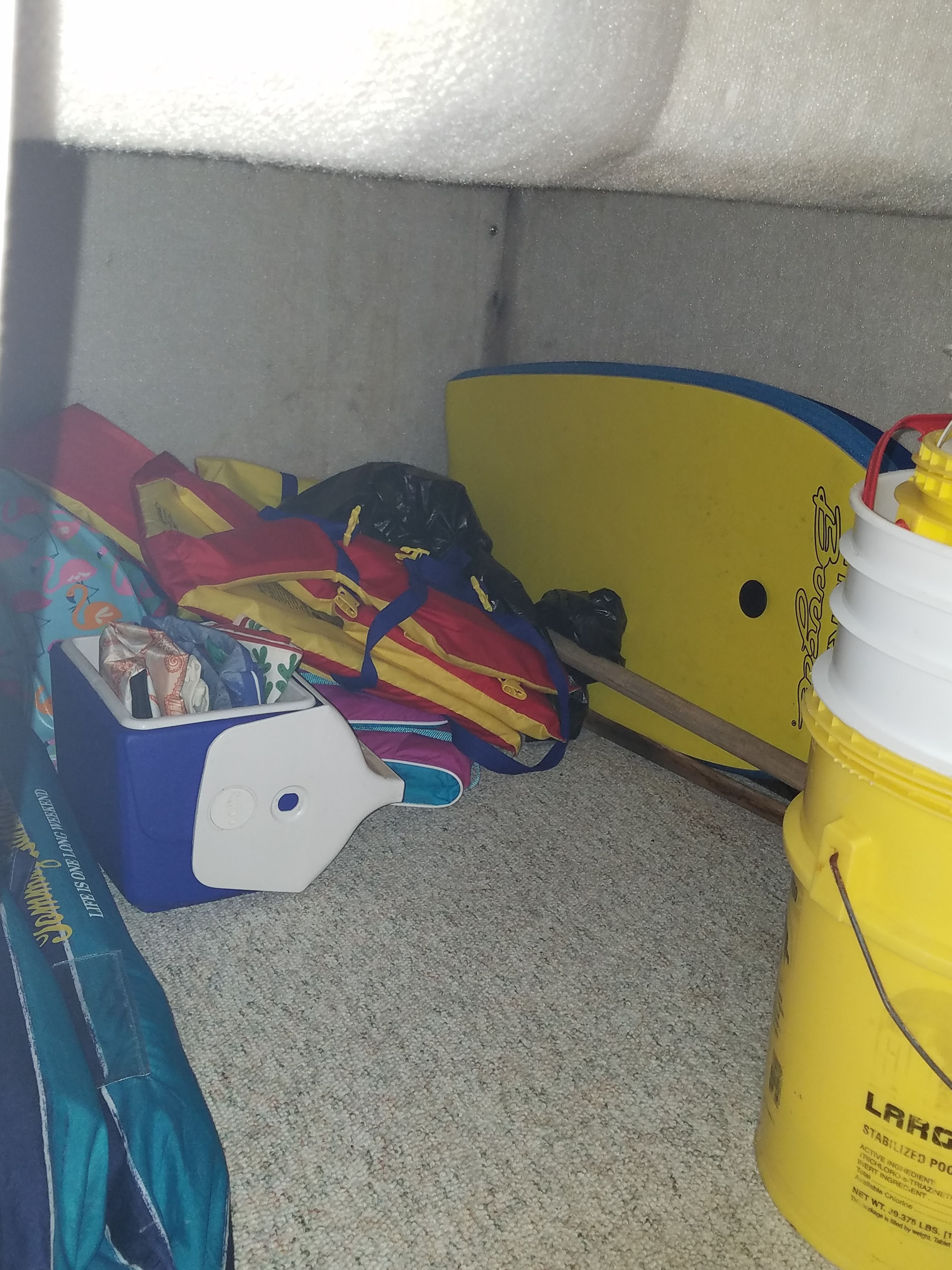 Interior of a boat with a cooler, life jackets, and a yellow bucket.