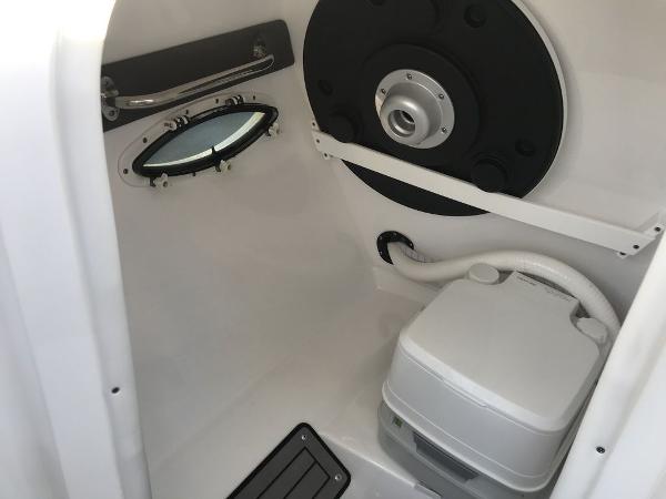 2020 Rinker 29QX BR boat interior with a compact toilet and porthole.