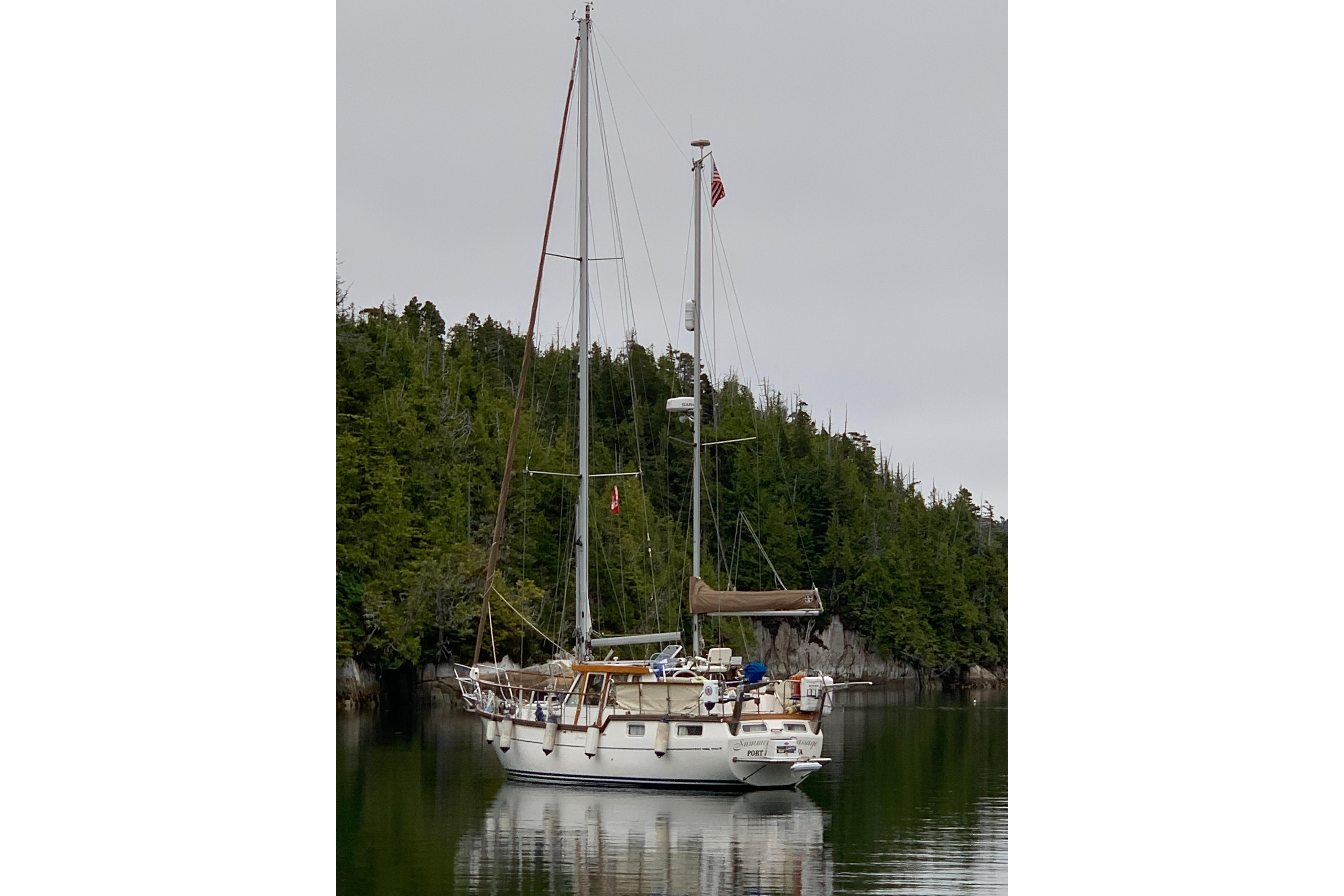 Sailing yacht Nauticat Staysail Ketch 2001 anchored in a serene forested bay.