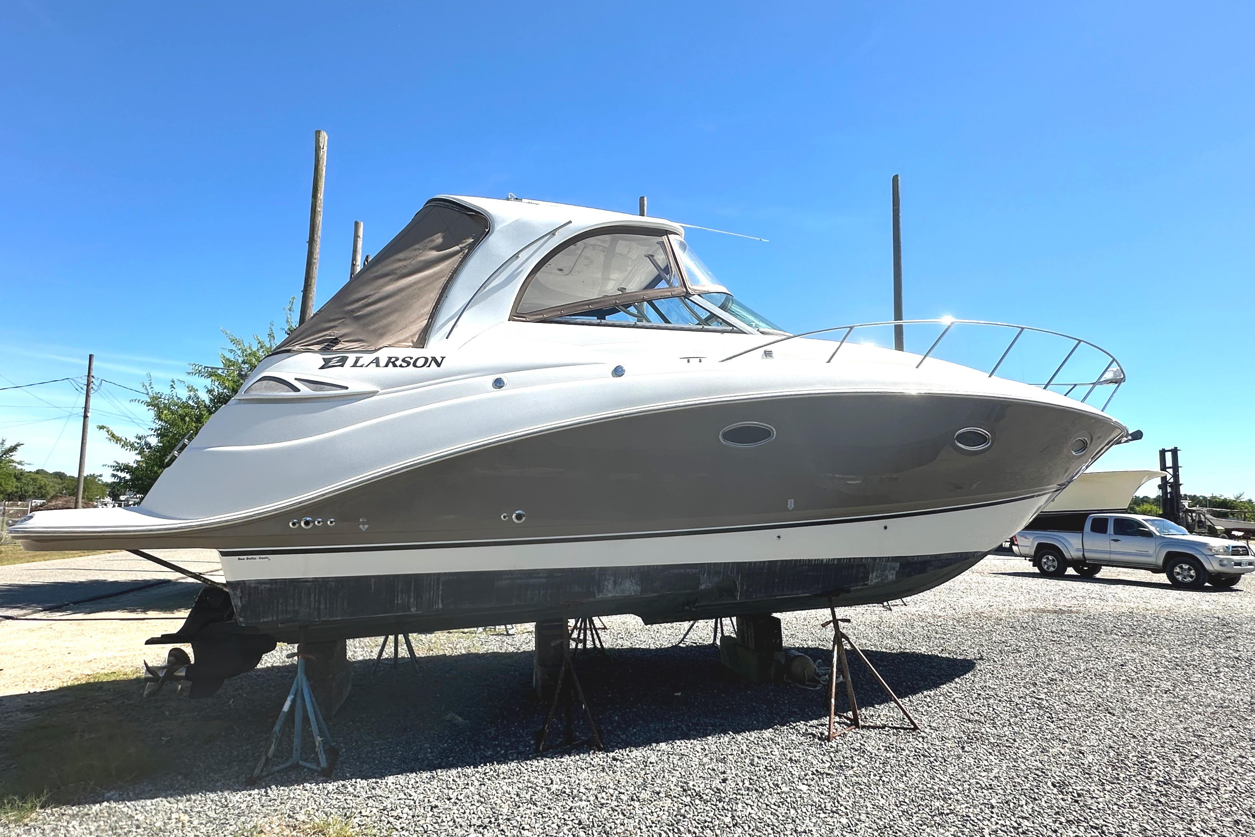 2006 Larson Cabrio 350 boat on stands, parked on gravel under clear blue sky.
