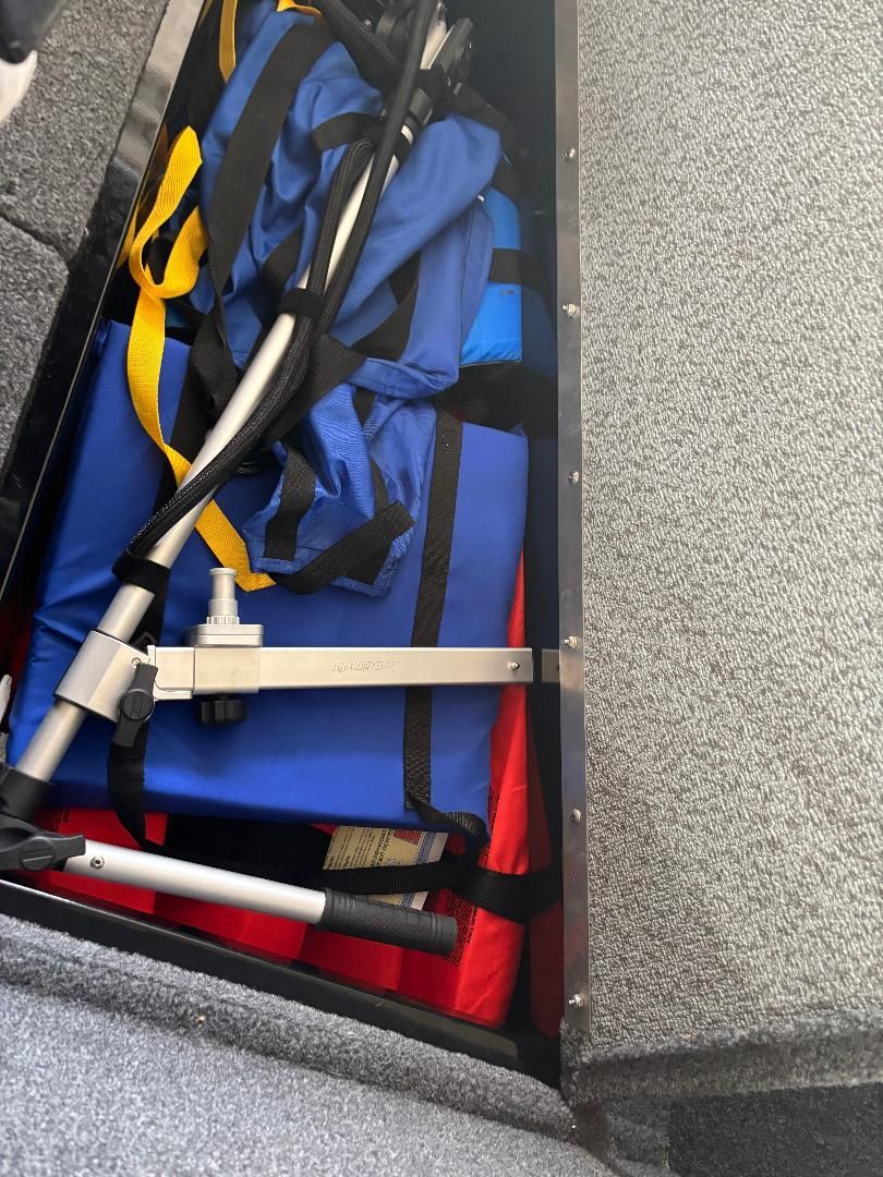 A storage compartment in the boat with blue and red life jackets and metal rods.