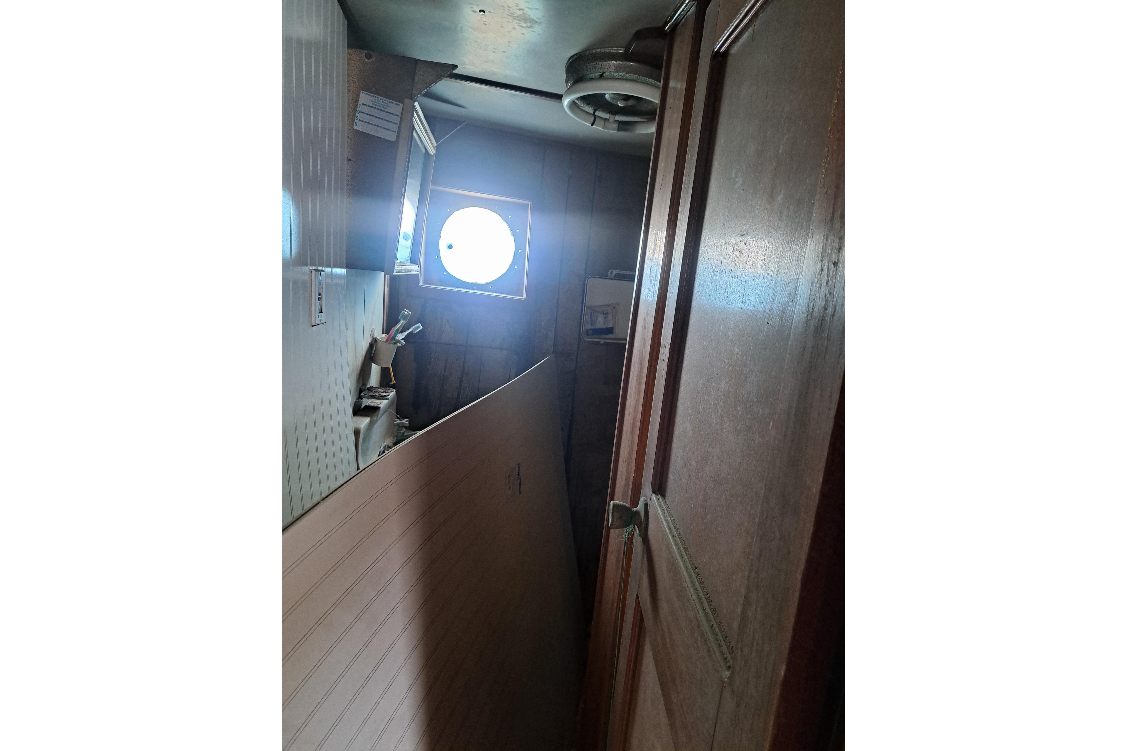 Narrow interior of 1979 Custom Steel Trawler Dragger with porthole and wooden door.