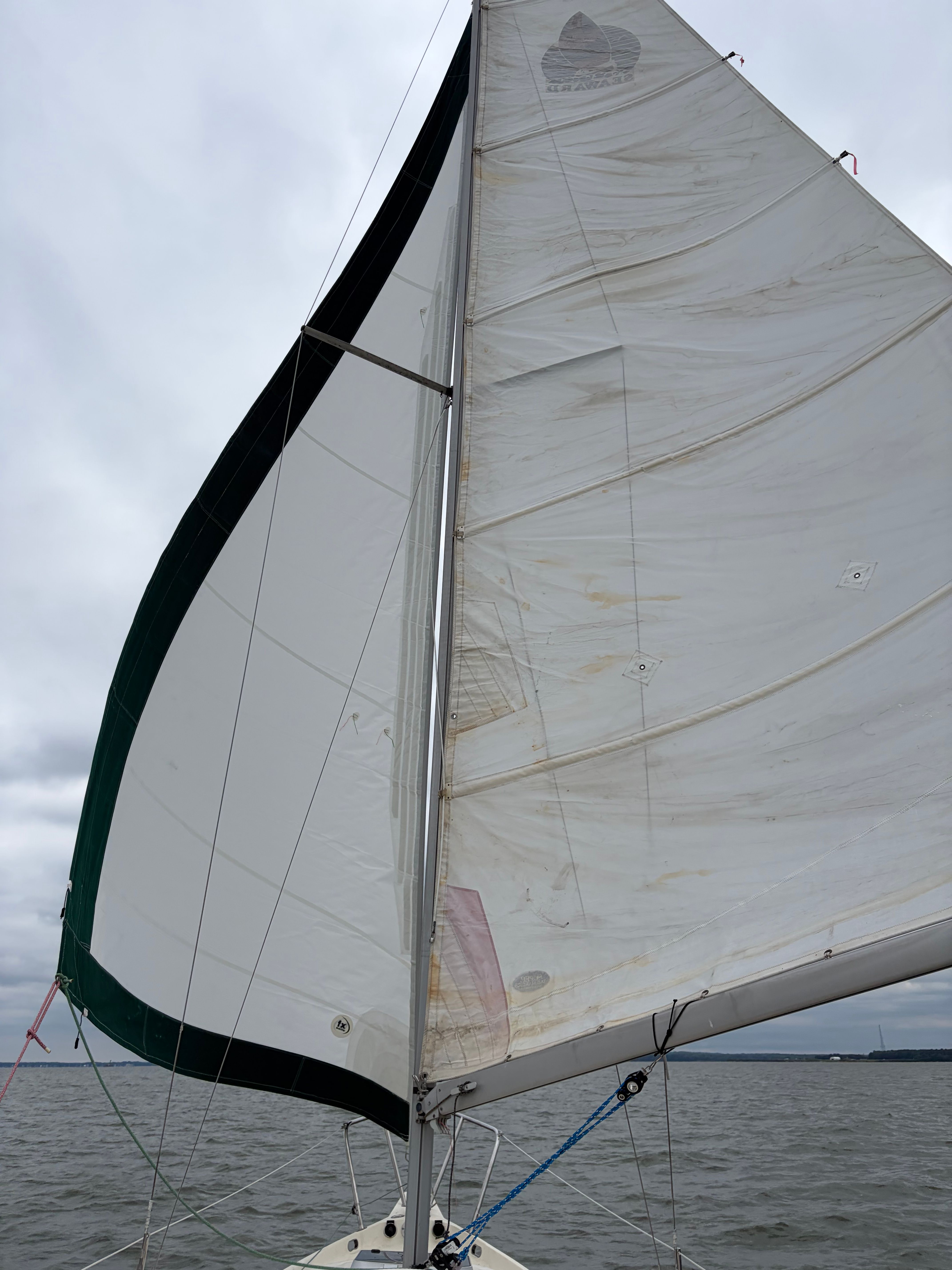 The image shows a sailboat's sail on the water under a cloudy sky.