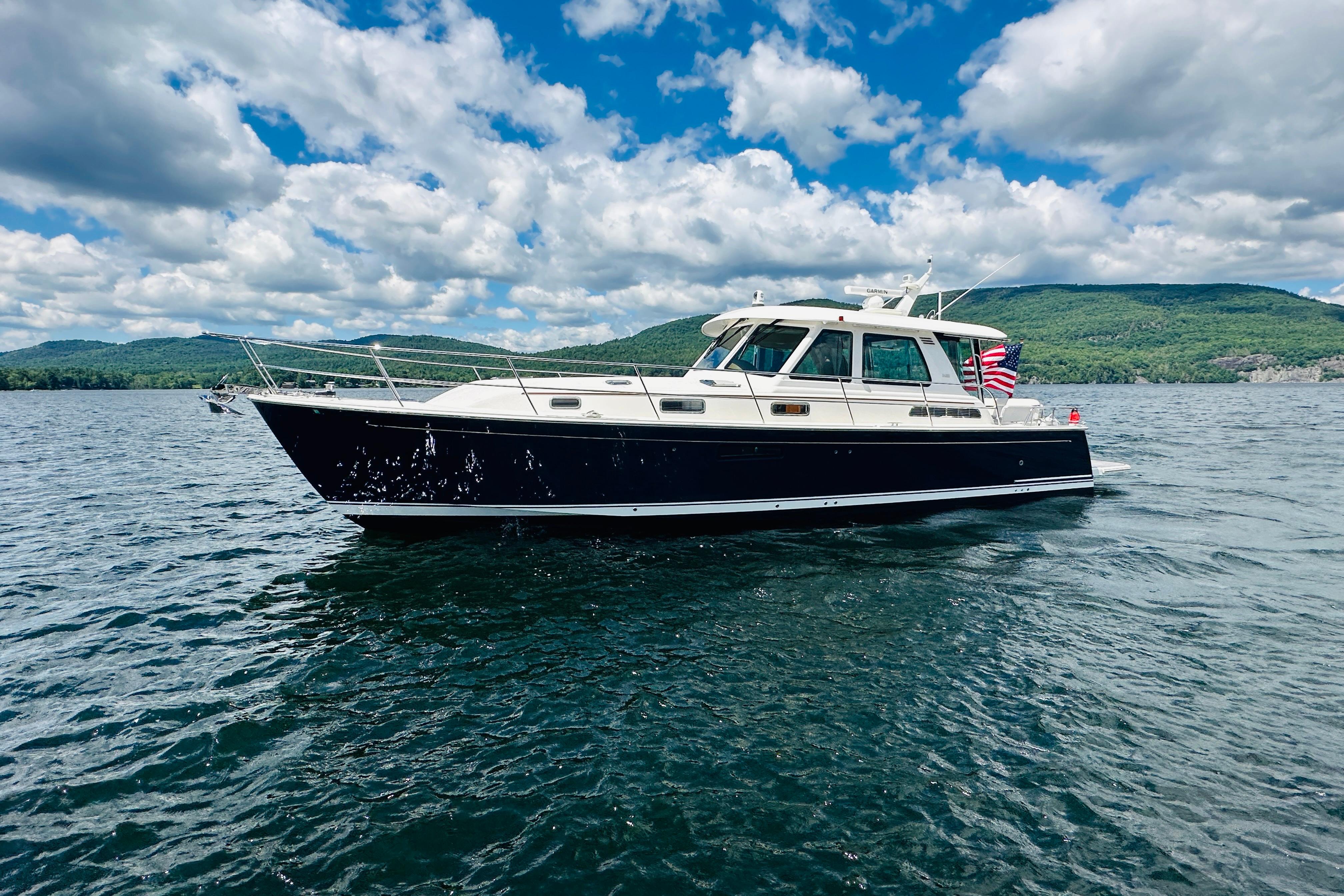2025 Sabre 48 Salon Express yacht cruising on a scenic lake under a partly cloudy sky.