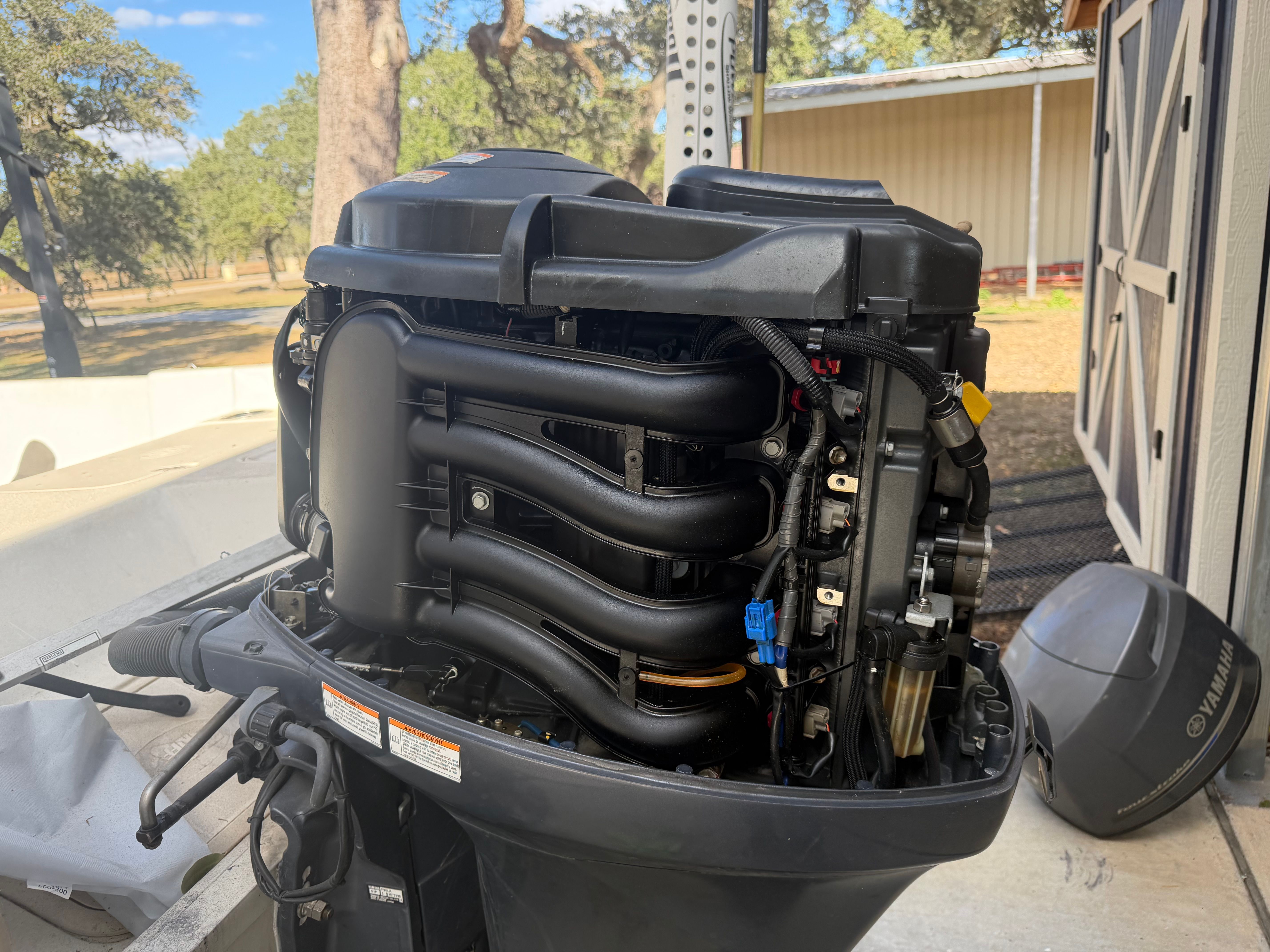 An outboard motor with exposed components, next to a shed outdoors.