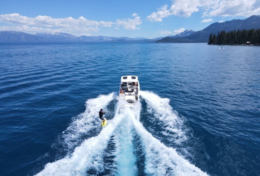 Chaparral 30 Surf from 2023 towing a wakeboarder on a calm lake with mountain views.