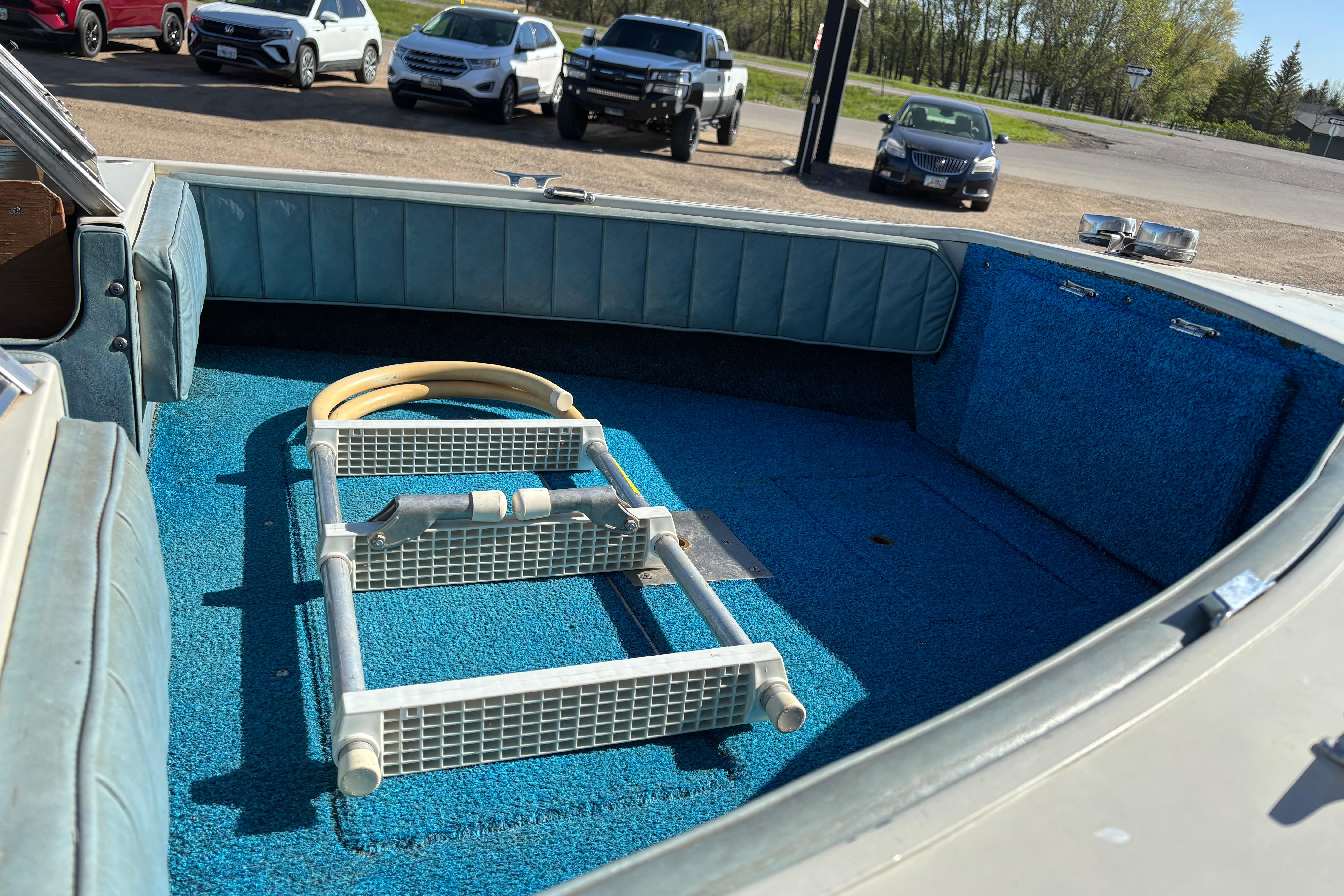 1983 Crestliner 16 boat interior with blue carpet and ladder, parked near vehicles.