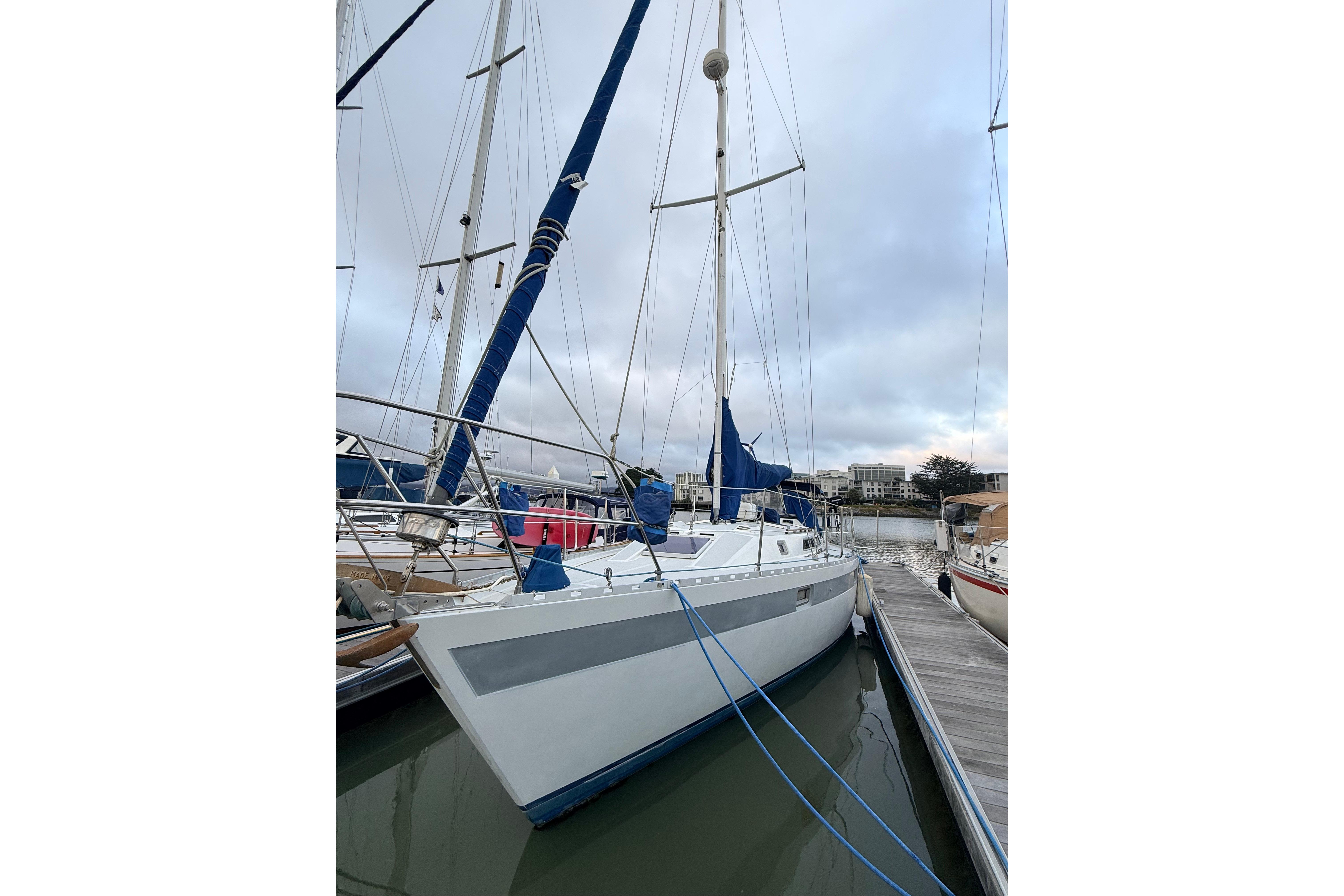 Sailboat Norseman 400, 1987 model, docked at marina with blue sails and overcast sky.