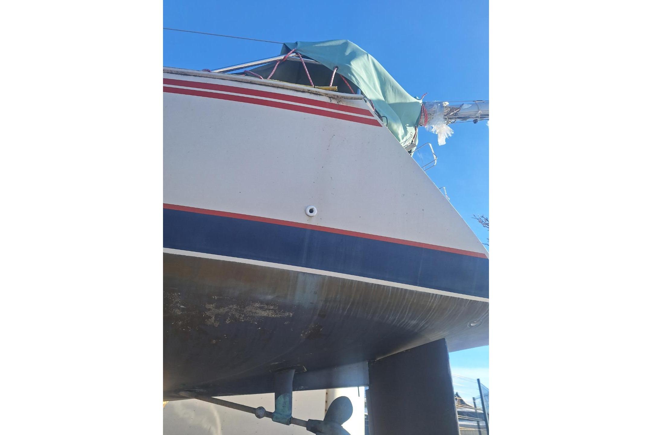 1983 Express 30 sailboat with red and blue stripes, covered deck, clear sky background.