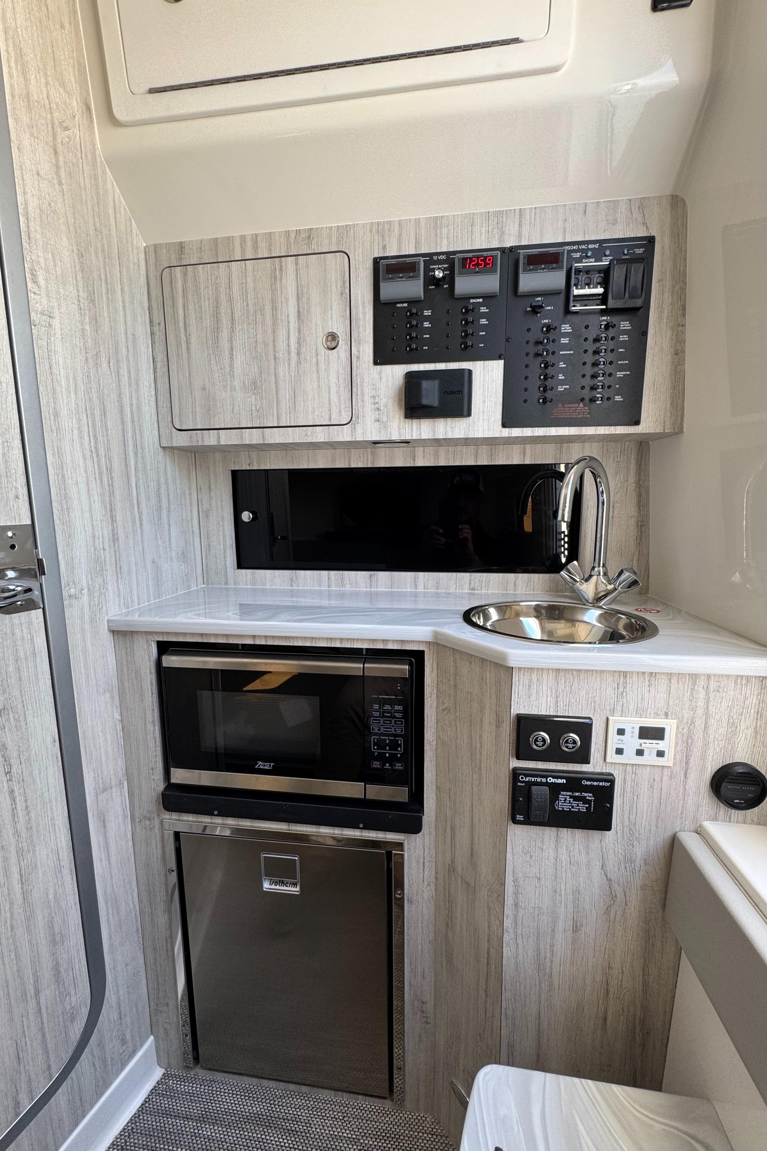 Compact kitchen area in a 2025 Regulator 37 boat with microwave, sink, and control panels.