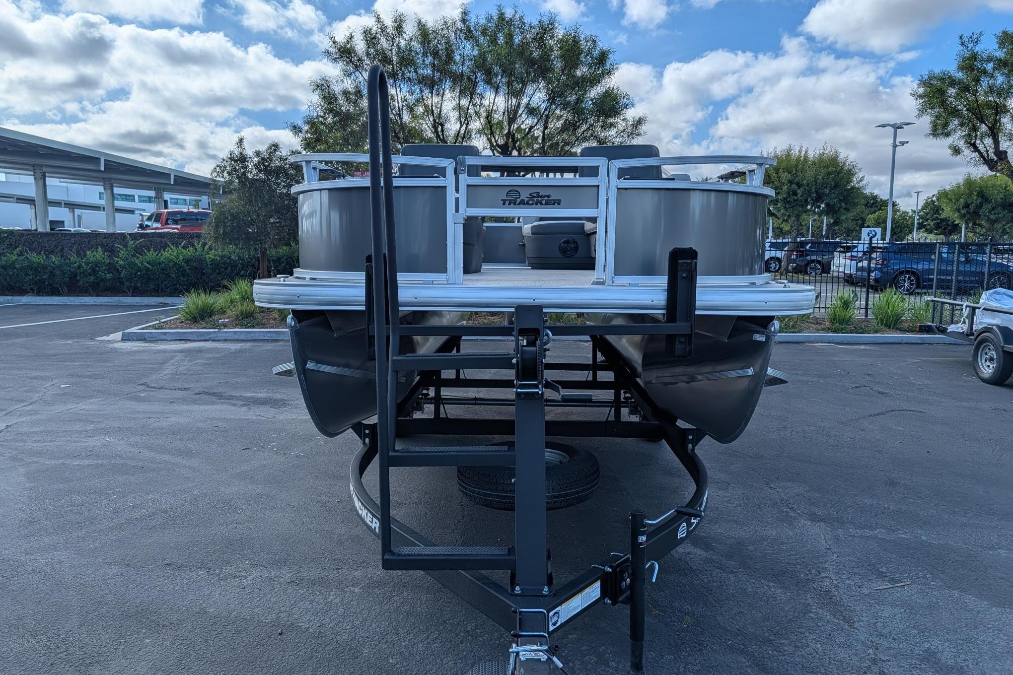 2026 Sun Tracker Bass Buggy 16 XL Select pontoon boat on trailer in parking lot.