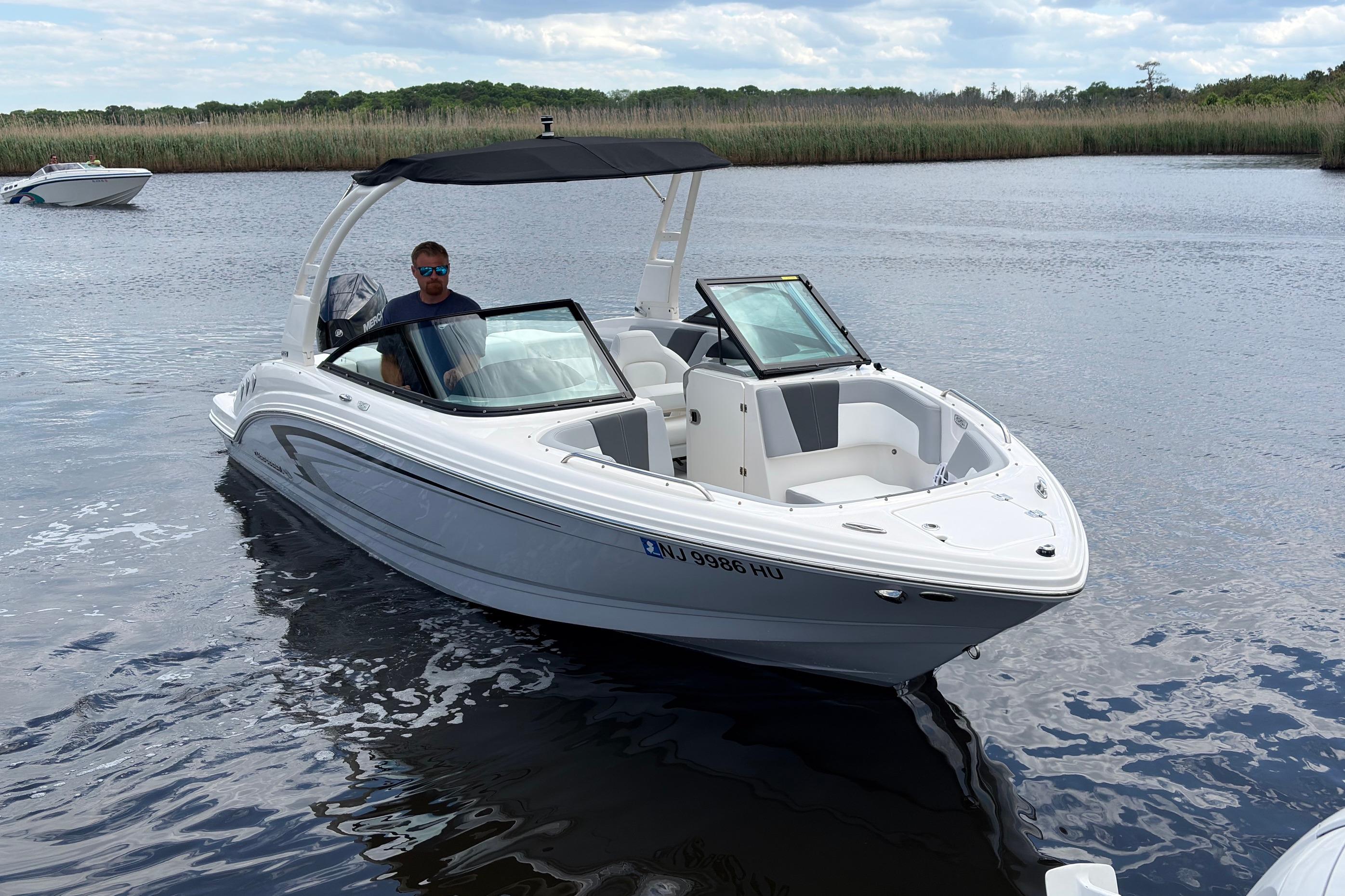 2026 Chaparral 23 SSi OB boat on calm water with a person at the helm.