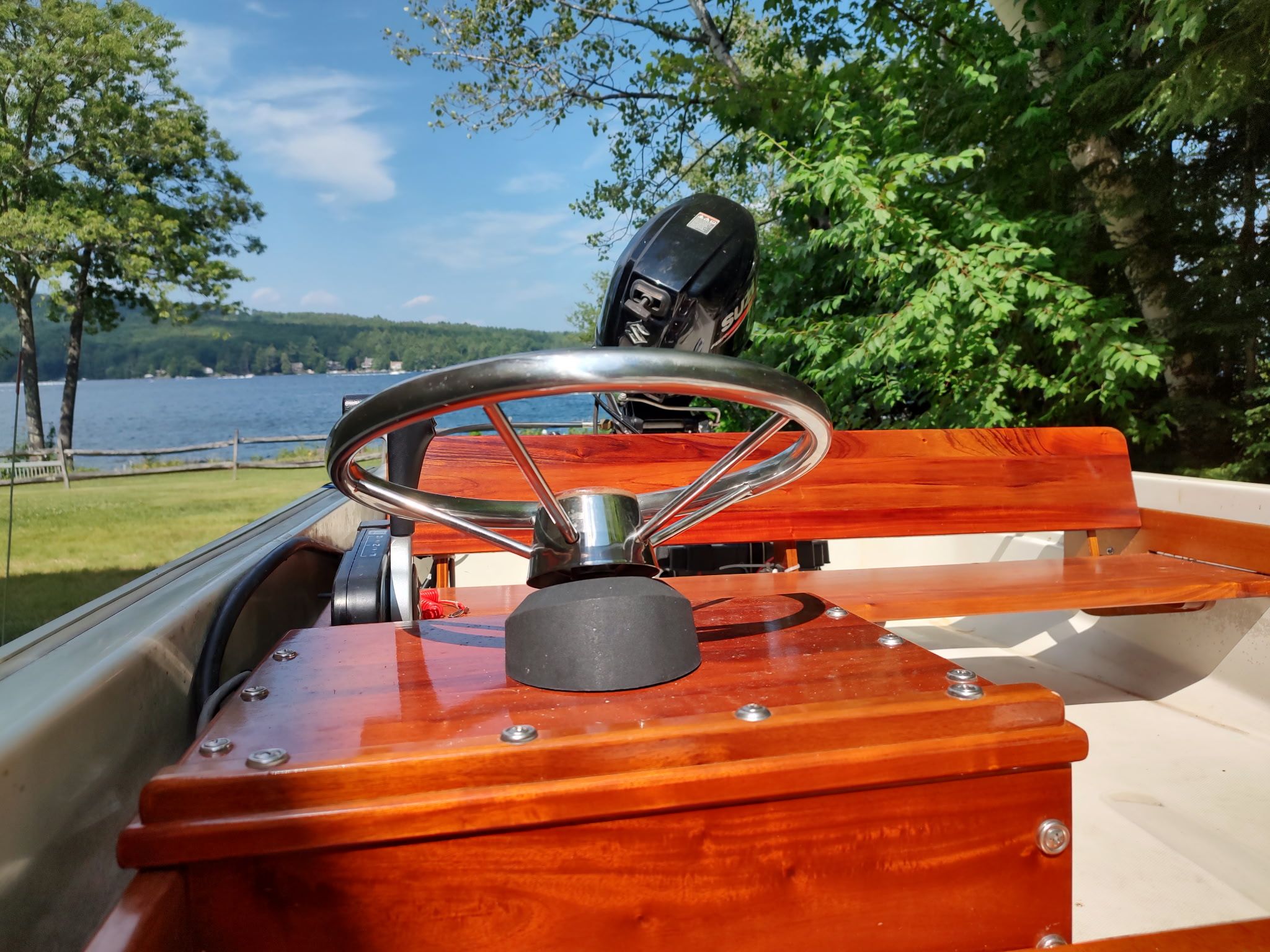 A 1987 Boston Whaler Sport 13 with wooden steering wheel and motor, parked by a lakeside.