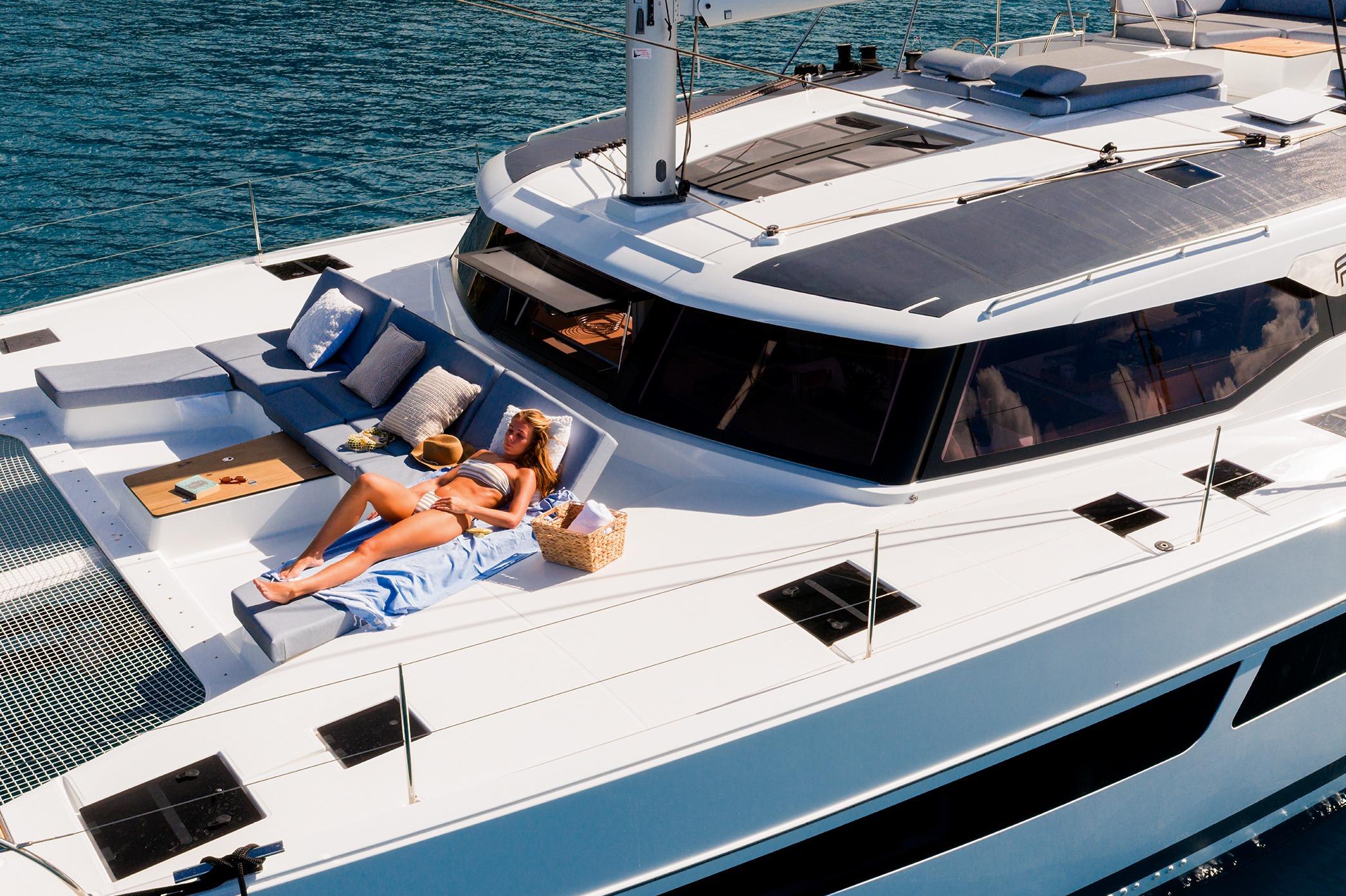 2026 Fountaine Pajot Aura 51 Catamaran with sunbathing area on deck, cruising in clear waters.
