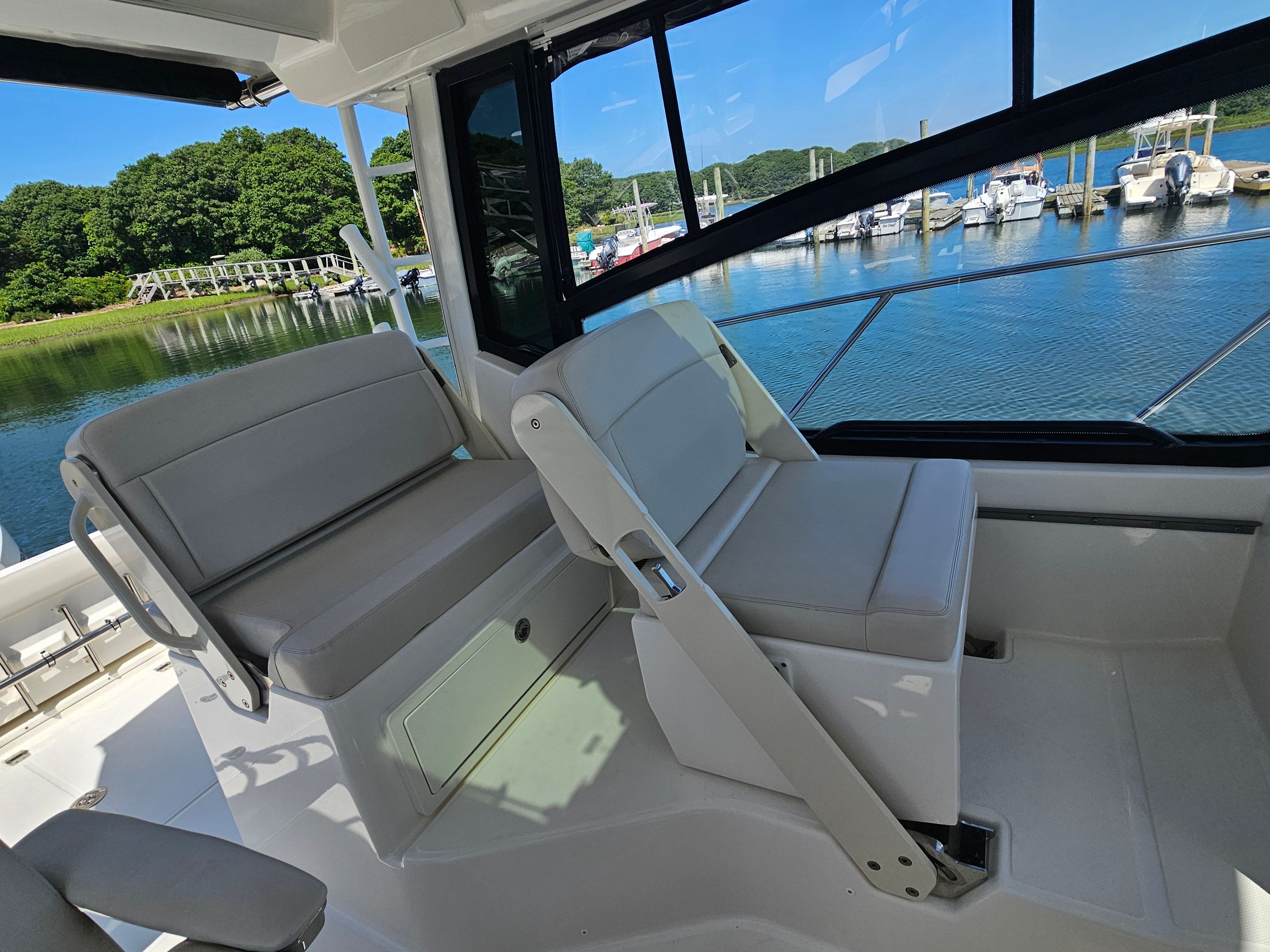 The image shows the cockpit of a Boston Whaler 325 Conquest with gray seats and a view of a calm marina.