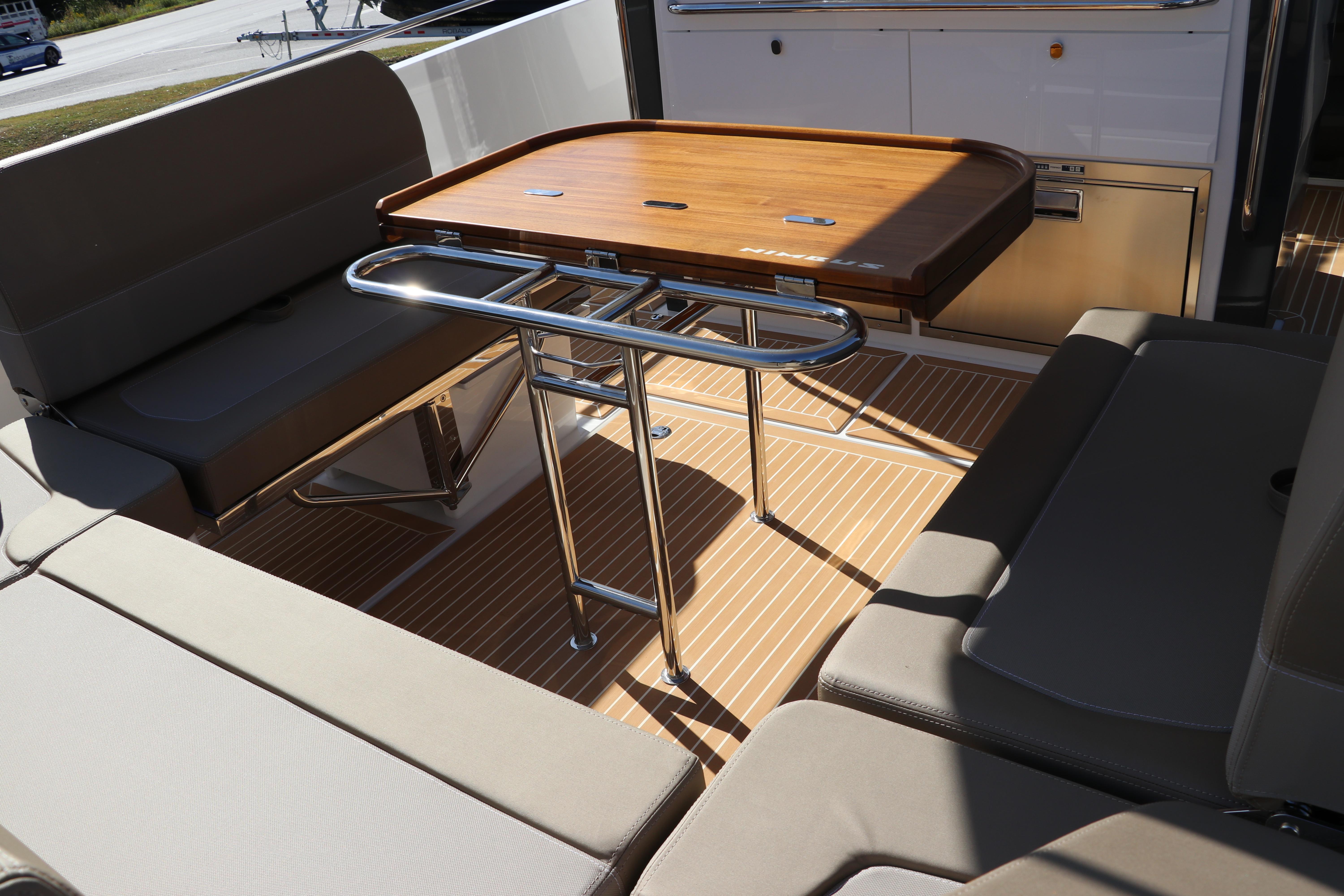 Luxurious seating area on 2025 Nimbus T11 boat with wooden table and cushioned benches.