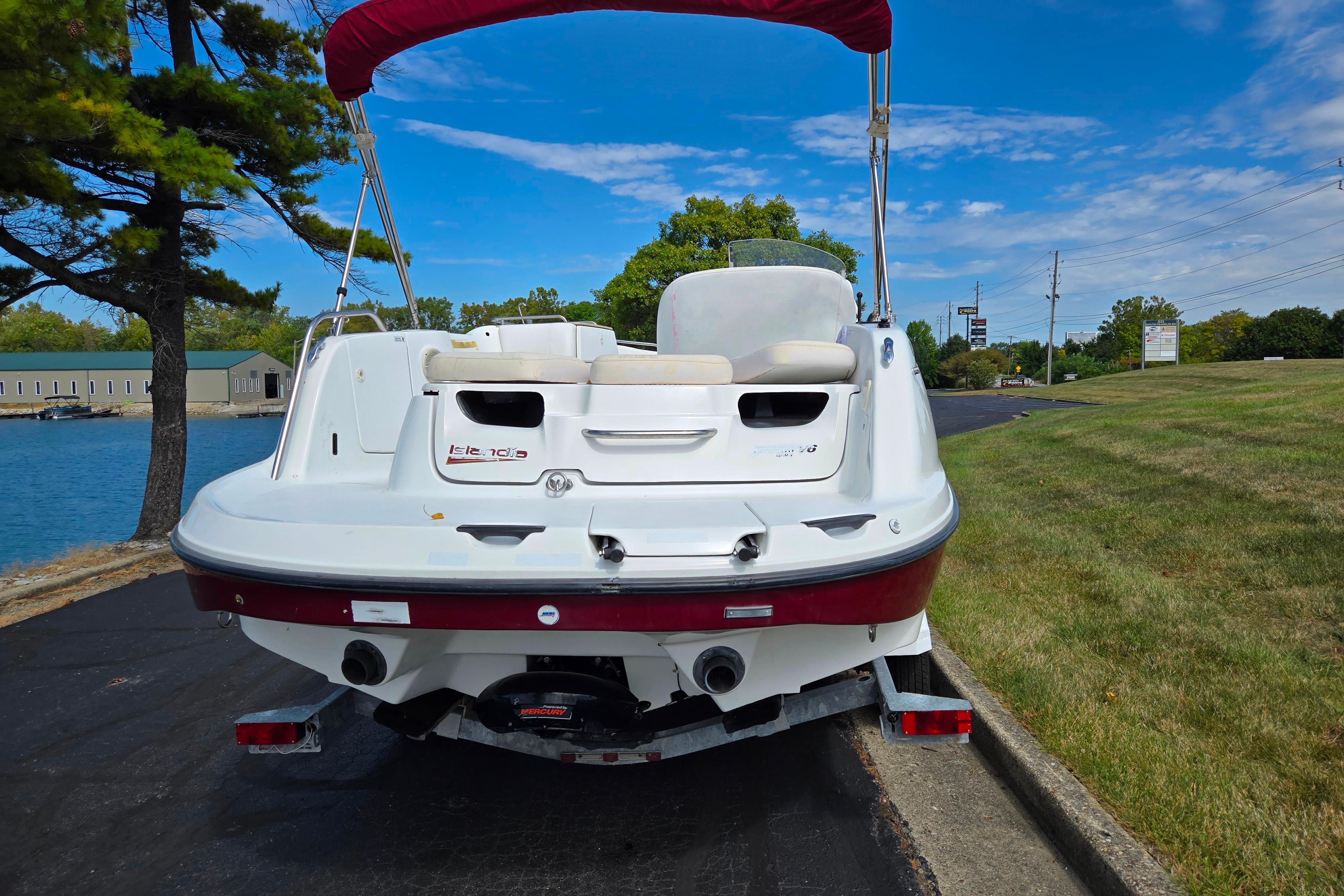 2004 Sea-Doo Islandia boat on trailer, parked near a lake under a clear blue sky.