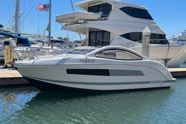 2024 Bracewell 25 boat docked at marina, sleek design, sunny day, American flag in background.
