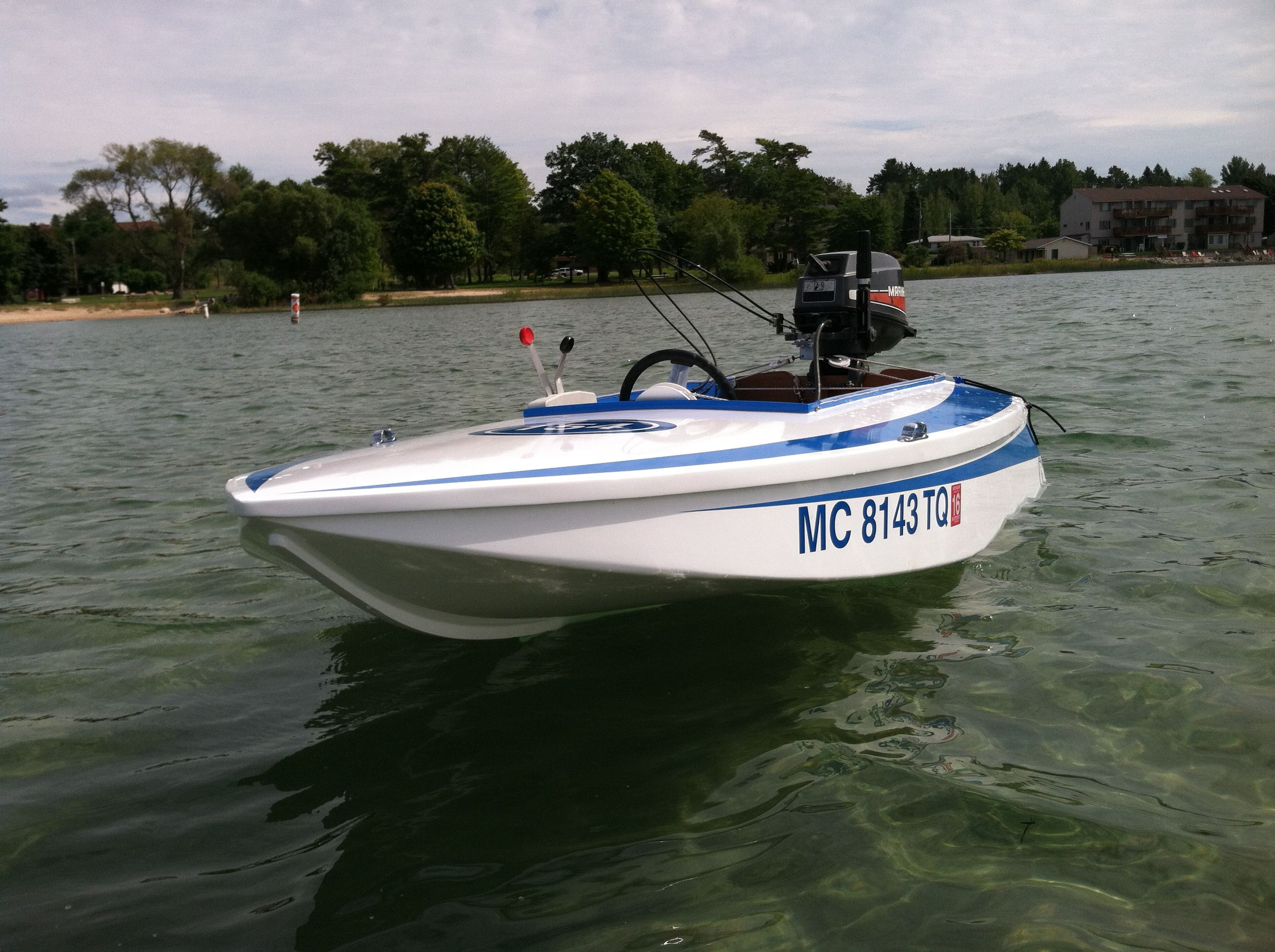 A white racing boat with blue accents floats on calm water near a beach.